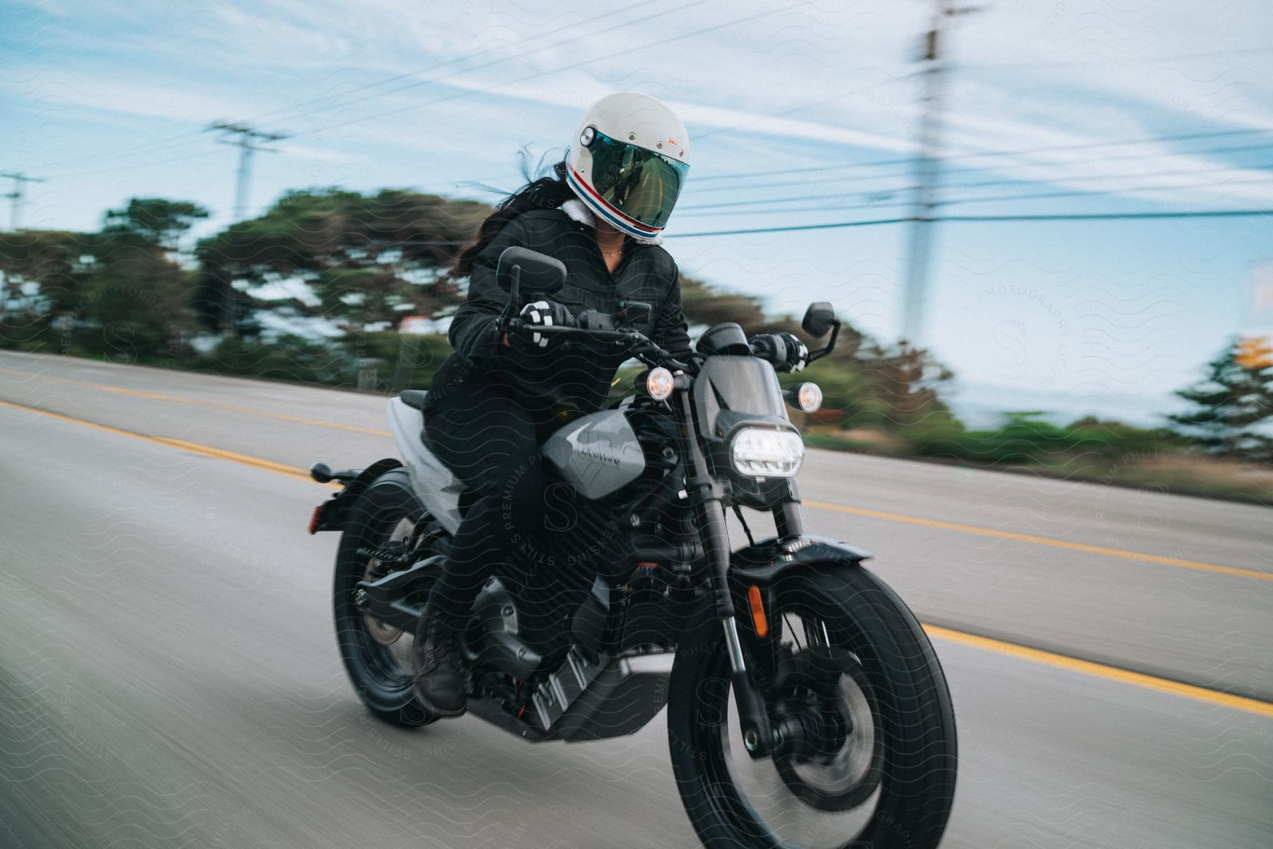 A motorcyclist wearing black clothing and a white helmet is riding a motorcycle at high speed on an open road.