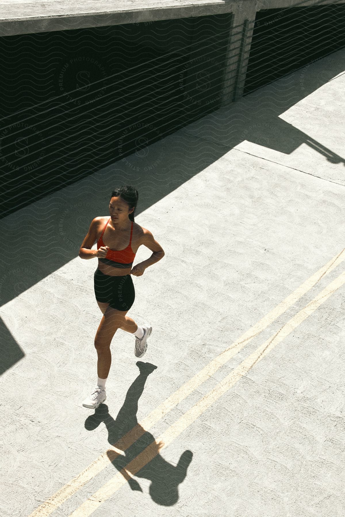 A woman with a ponytail, red top, and black shorts runs down the street under the shining sun.