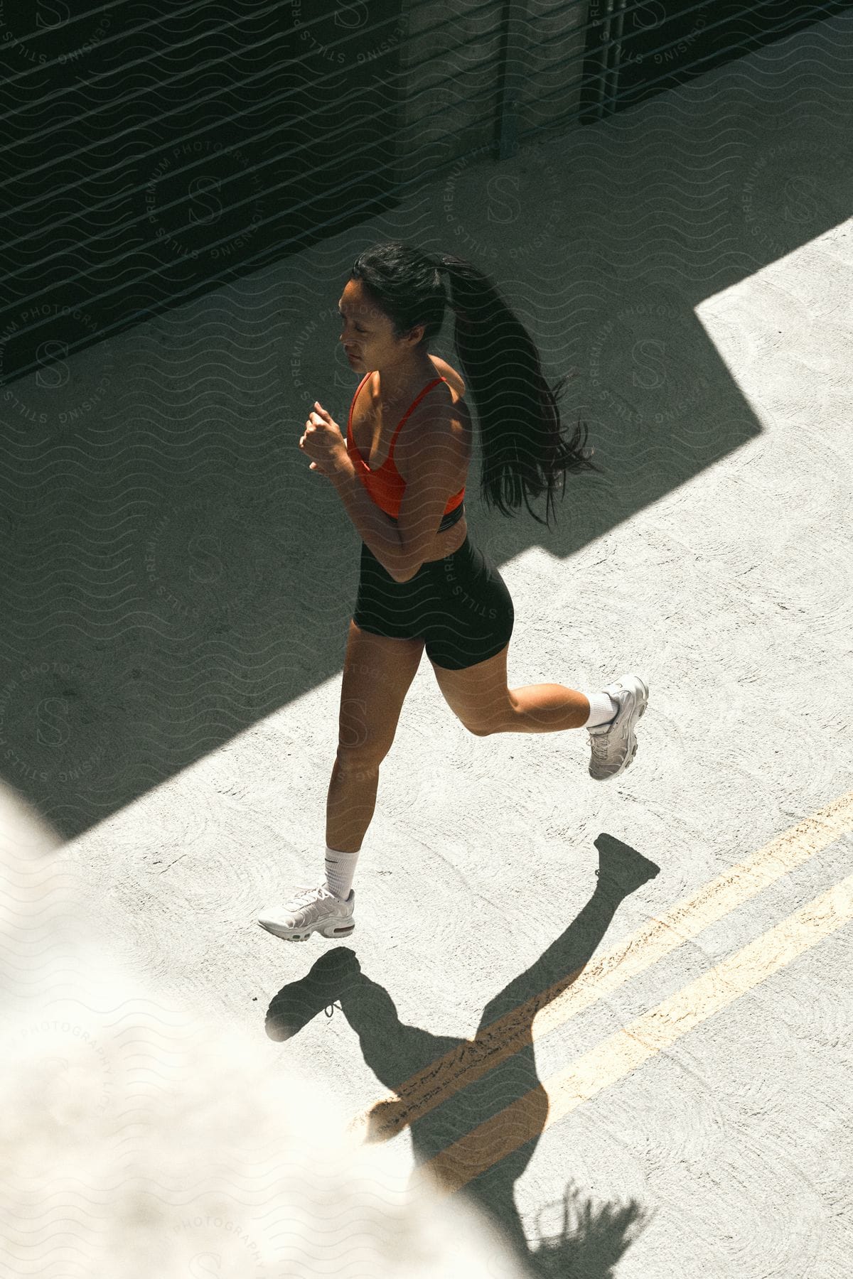 A woman with a ponytail, red top, and black shorts runs down the street under the shining sun.