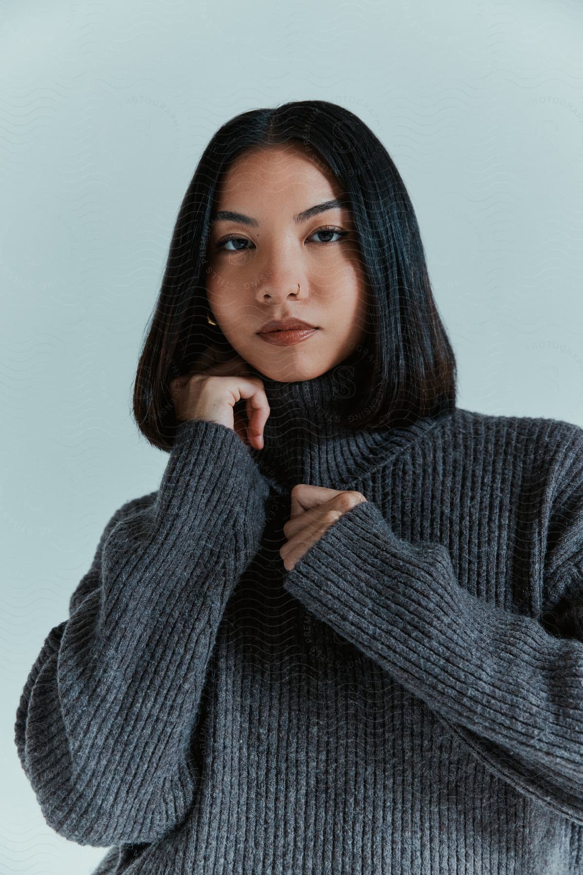 Woman with straight, shoulder-length hair wearing a gray ribbed sweater with her hands near her face.