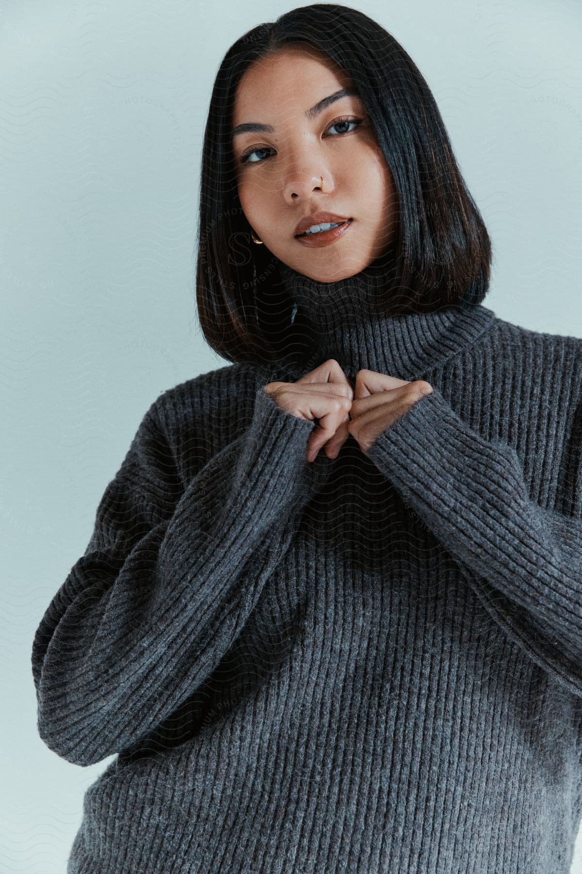 Young woman wearing a gray turtleneck with her hands crossed in front of her chest.