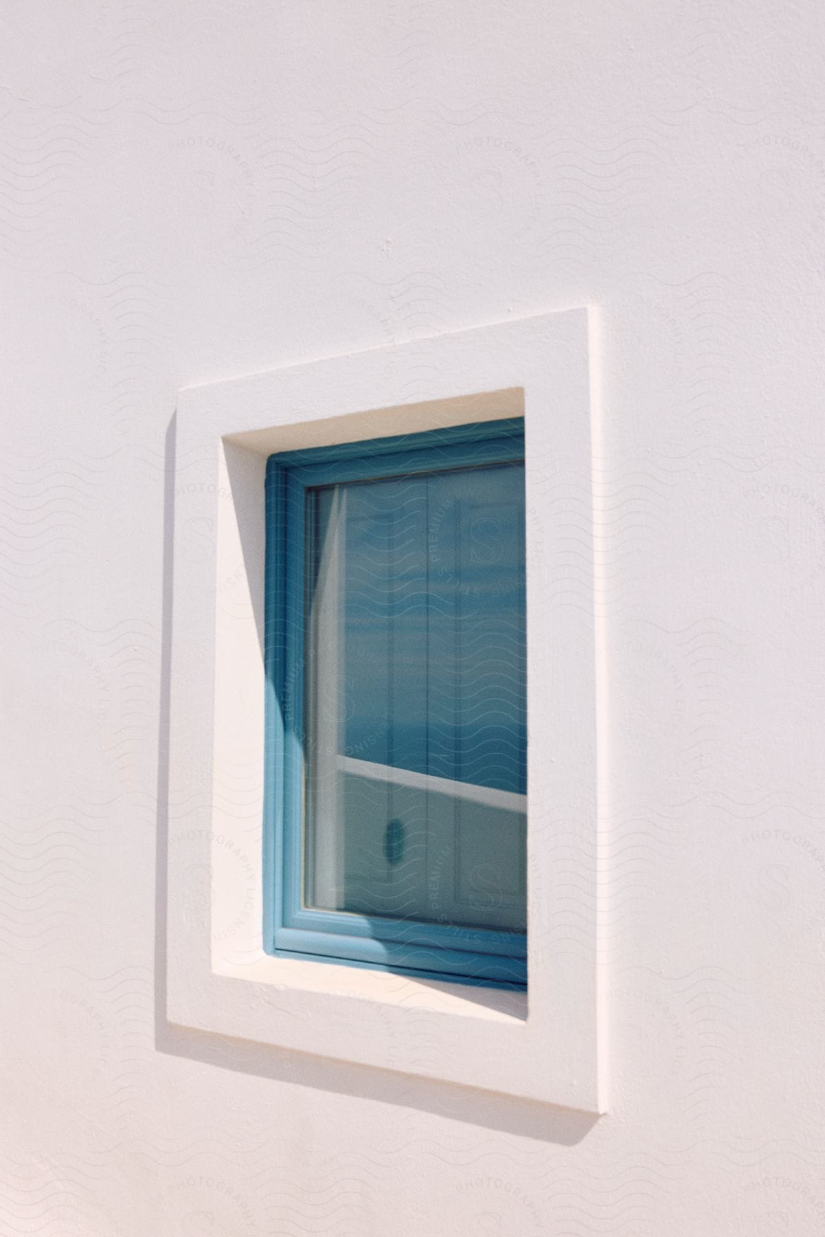 A white, three-dimensional square window frame with a blue window set into a white wall.