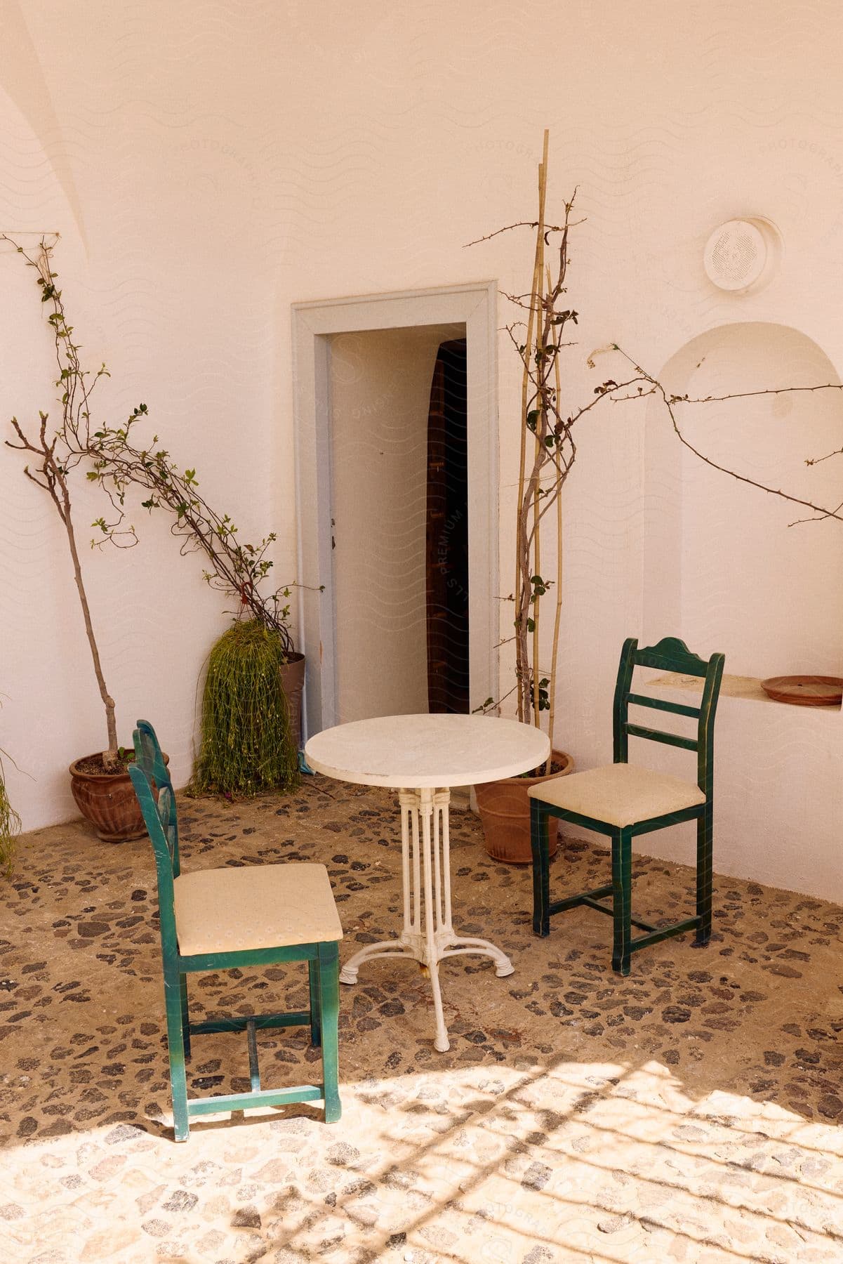 a courtyard, showing a round table and two chairs with potted plants nearby.