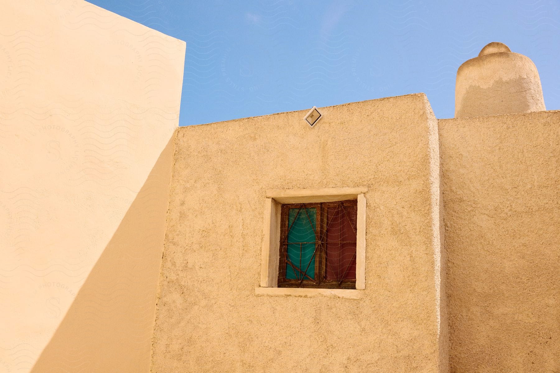 Exterior architecture of a sand-colored wall with a small closed colored window