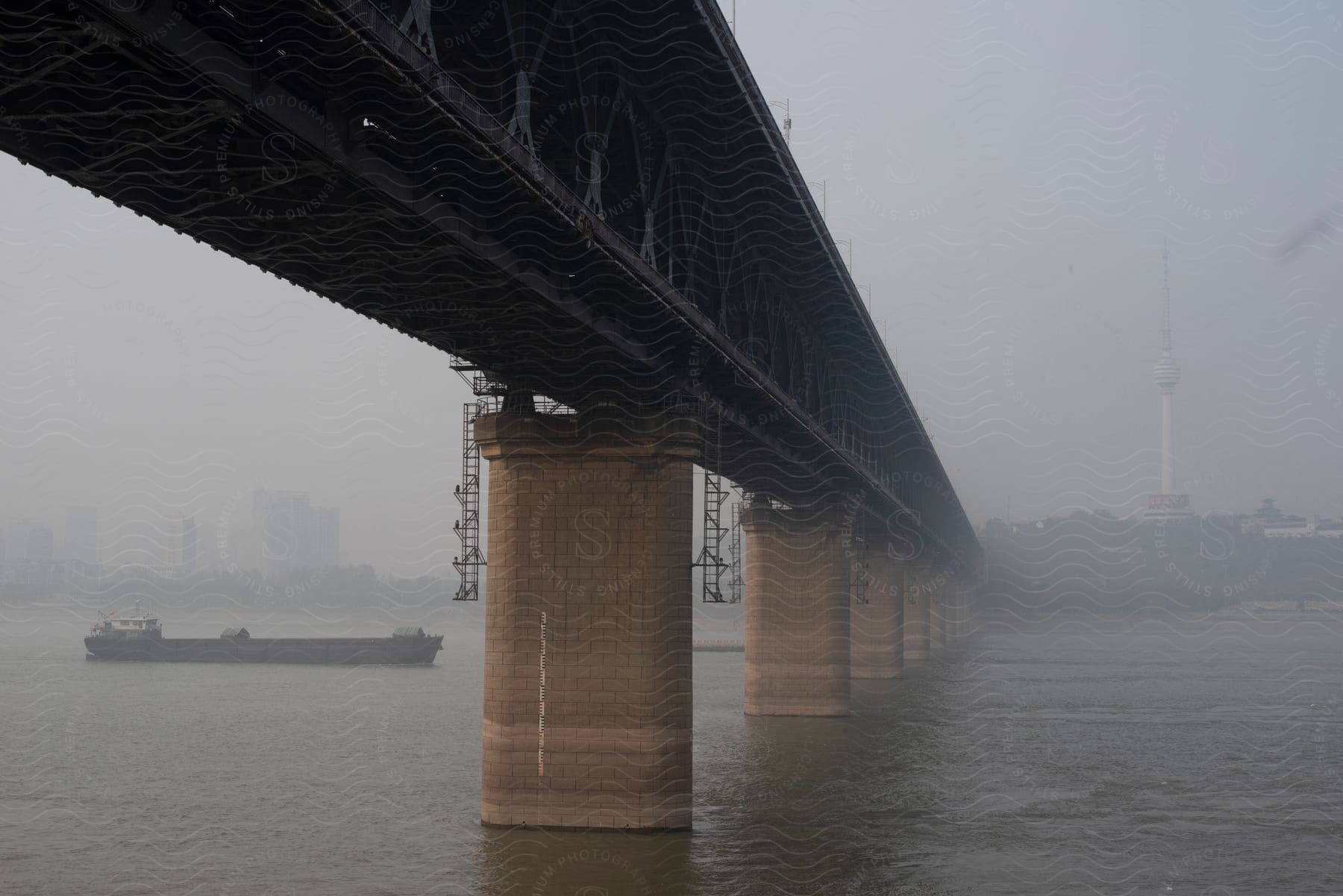 Wuhan Yangtze River Bridge over the sea with a cargo boat in the background on a foggy day.