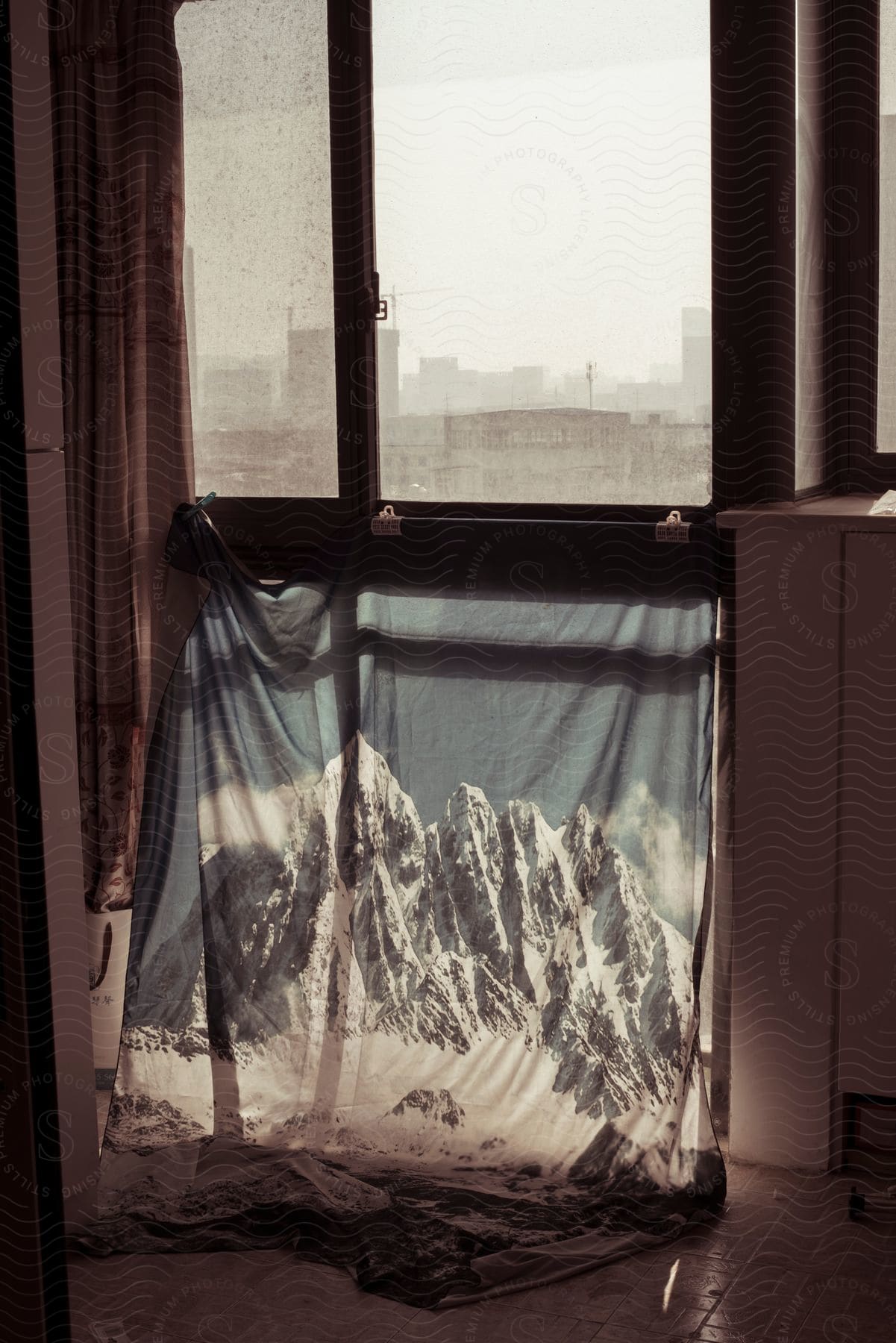 Interior design of a window reveals a cityscape while a fabric printed with snowy mountains creates a visual contrast with the sunlight.