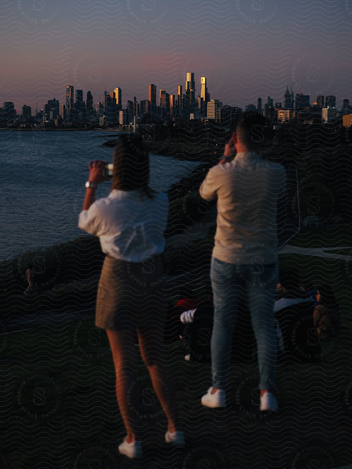 People are taking pictures of a big city along the coast with tall towers and skyscrapers on the skyline