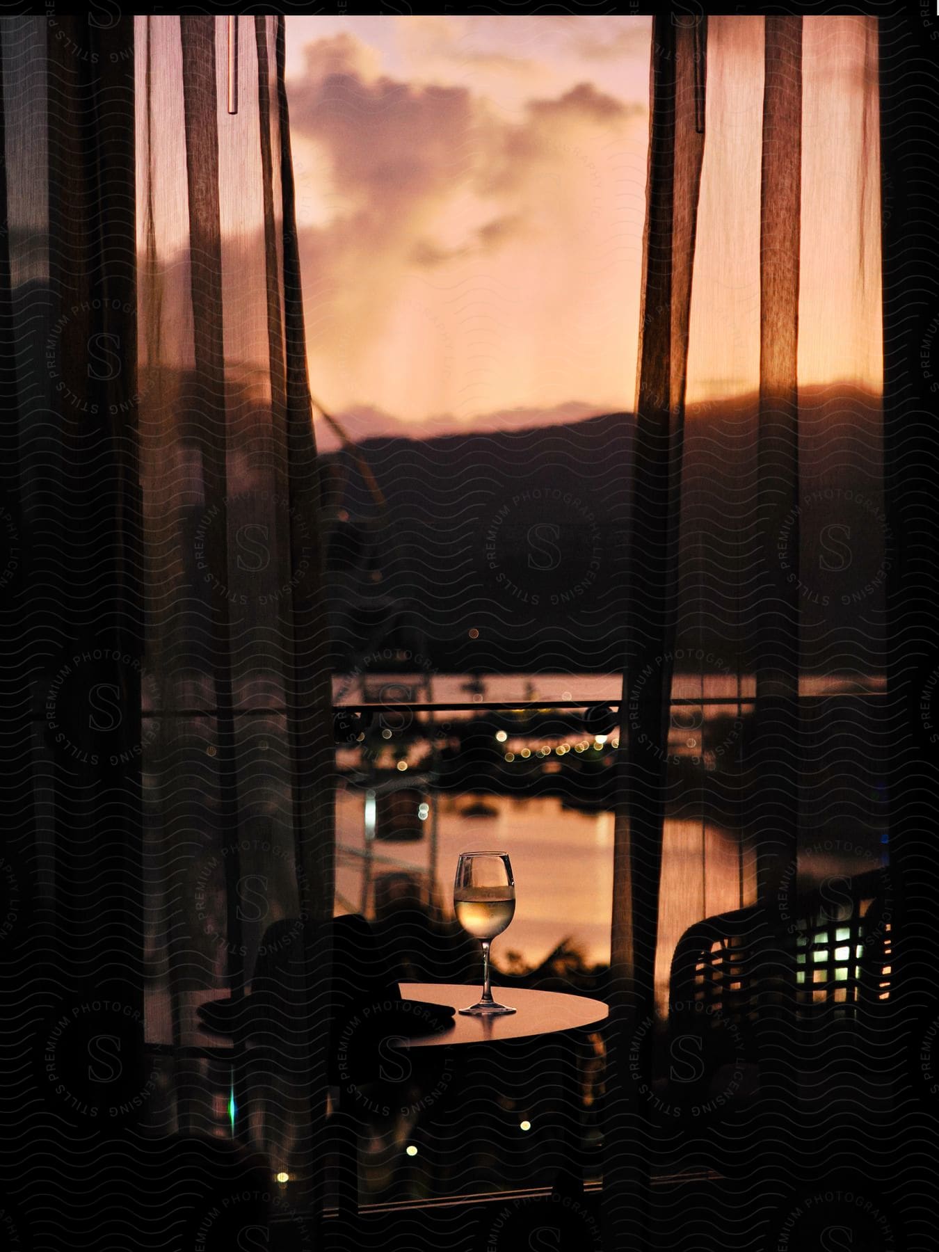 A glass of wine sits on a table in a room that overlooks a river at sunset.