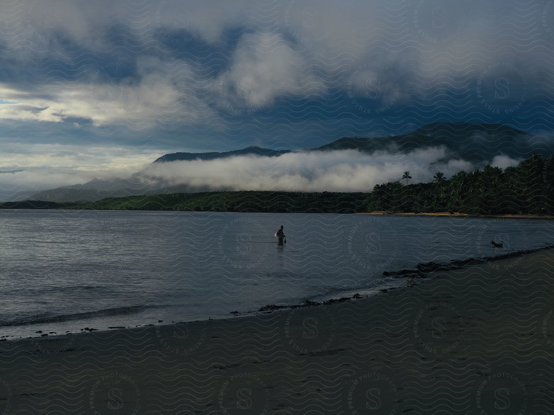 A person stands in the ocean at the beachside during the evening.