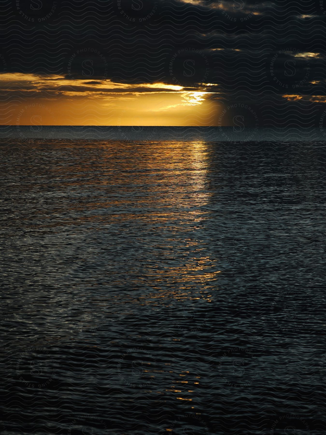 Sunrise over the ocean with sunlight reflecting on the water under a partly cloudy sky.