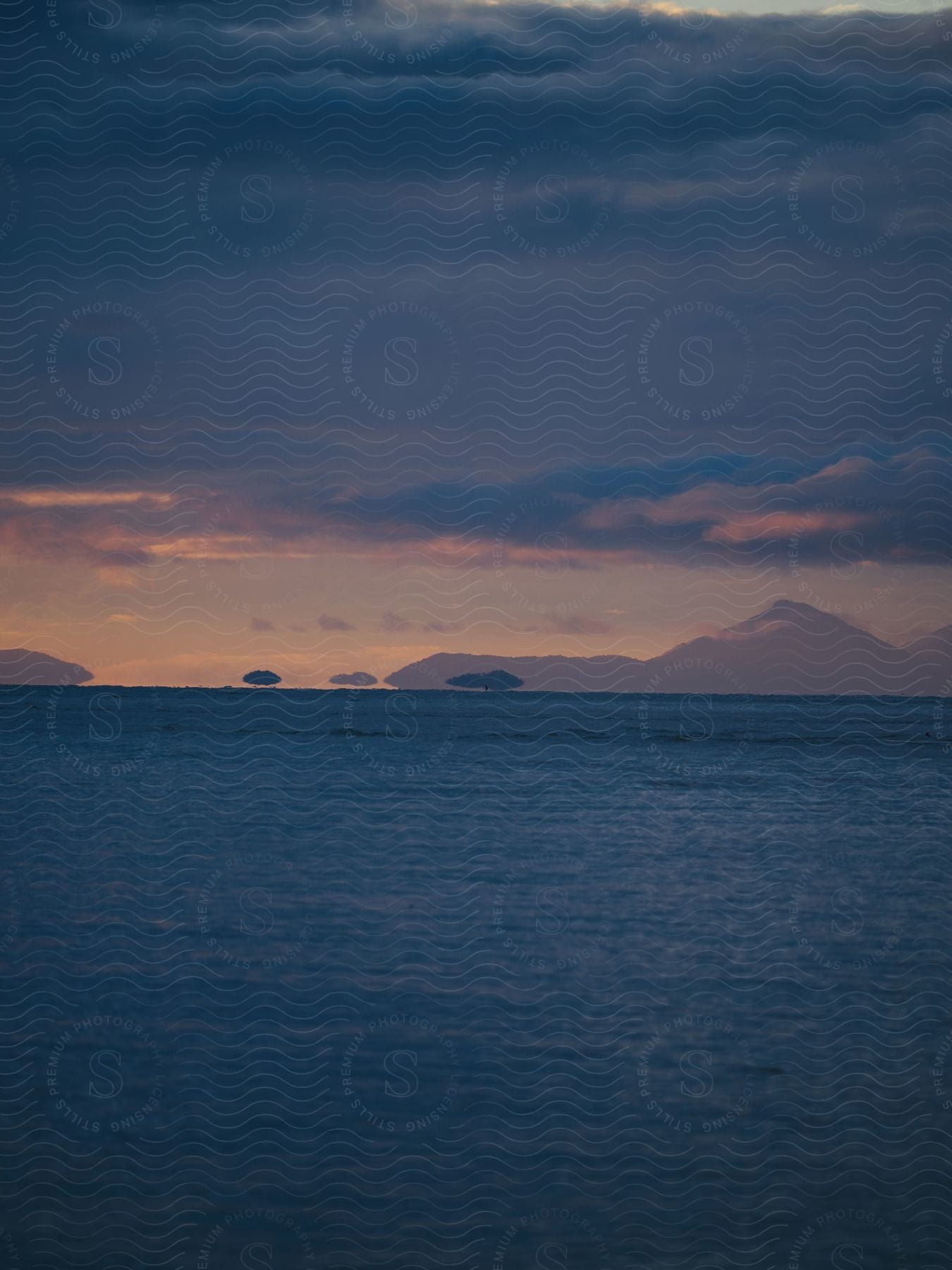 Clouds float over the open sea with mountains in the distance