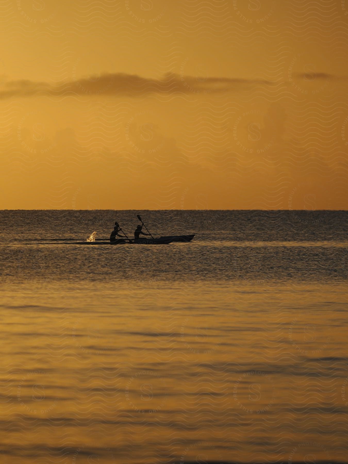 Two people paddling canoes under a yellow sunset sky