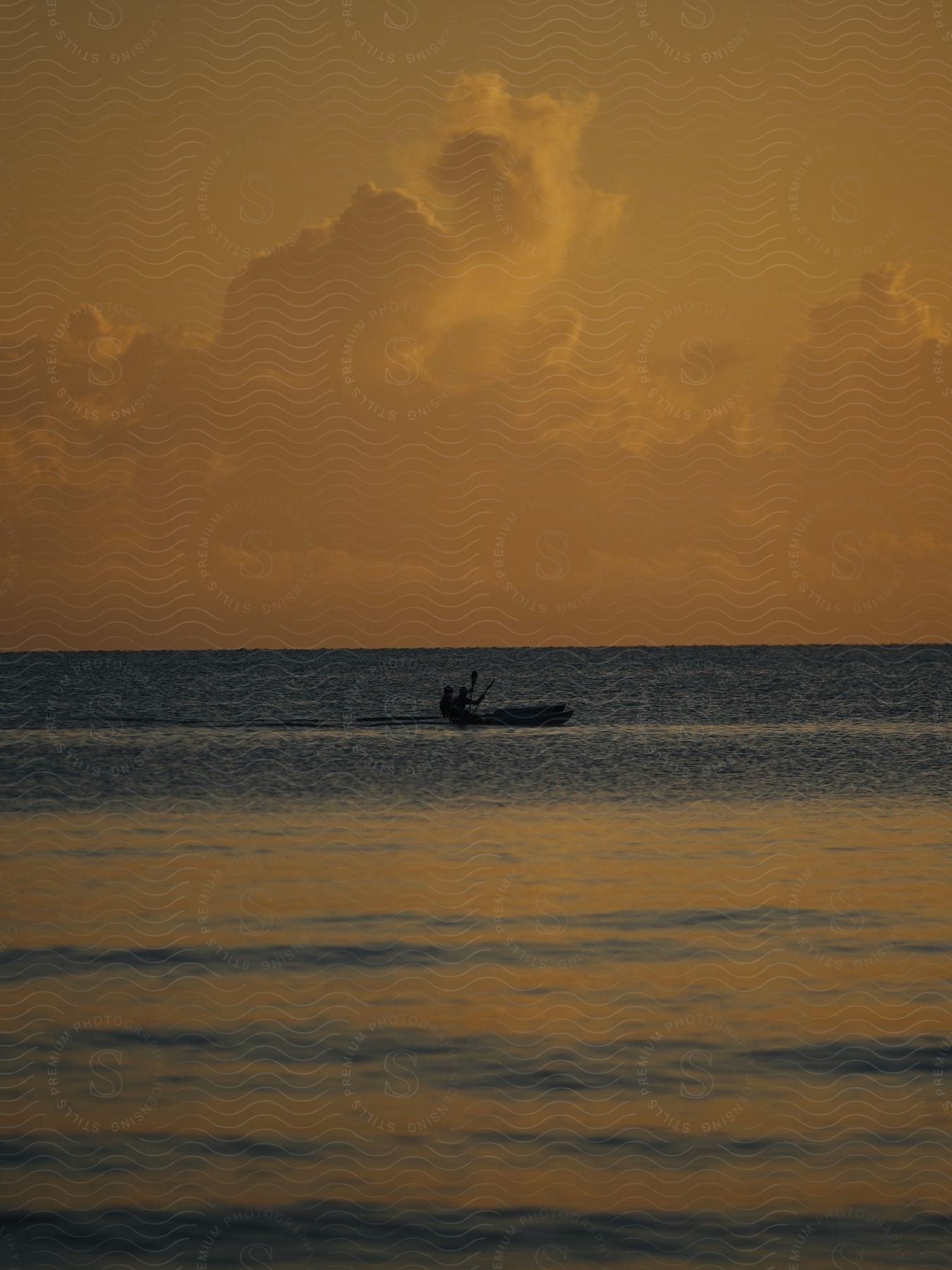 People are paddling canoes as the sun sets over the ocean. The sky is tinged with yellow and orange, creating a serene and peaceful atmosphere.