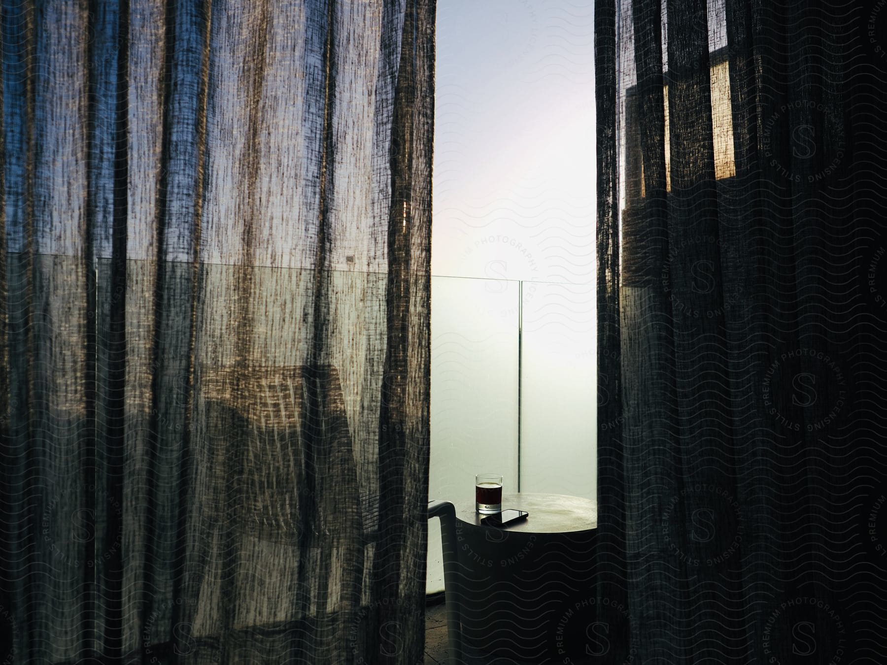 View through open curtains of a glass of water on a small round table outside