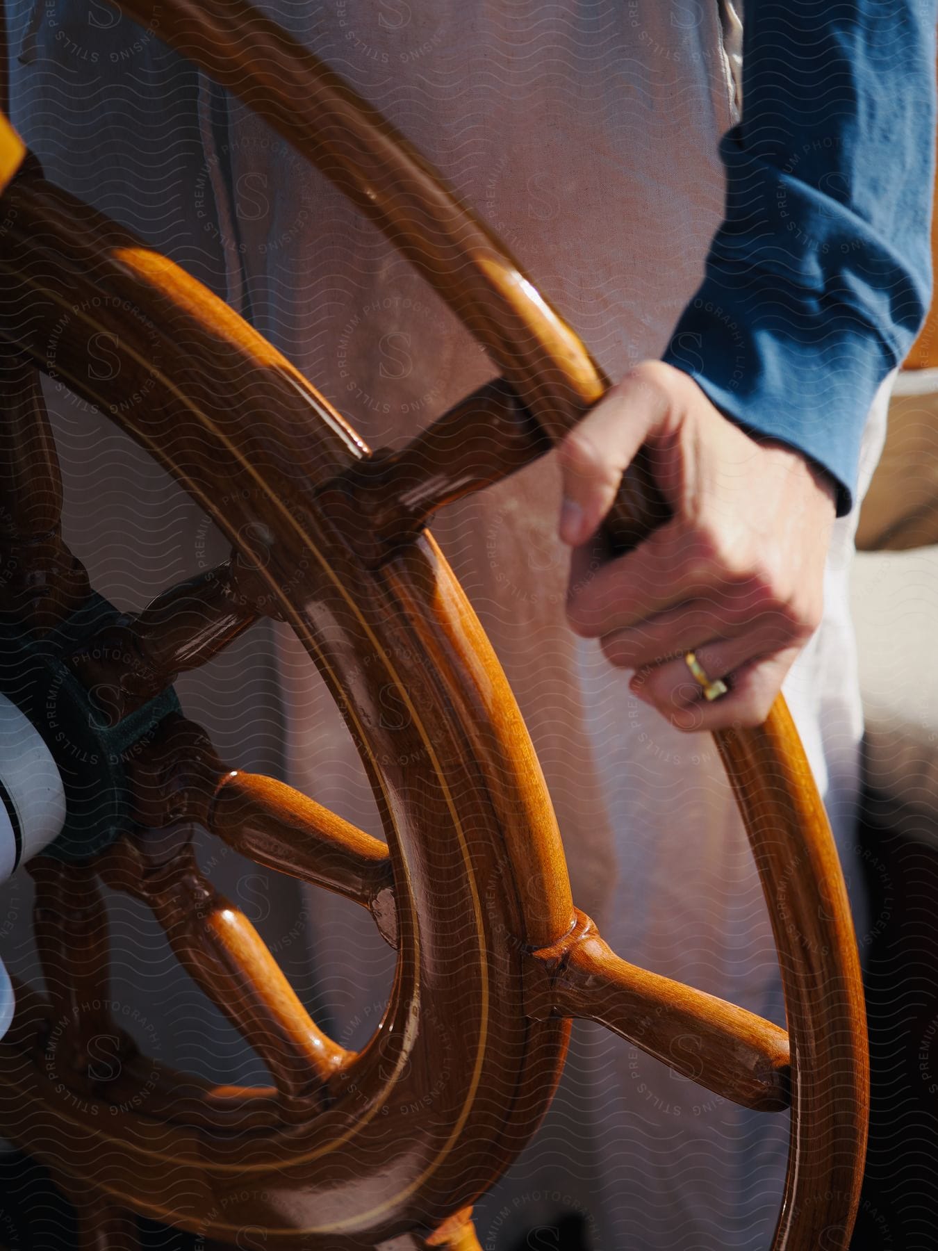 Woman wearing a ring stands and holds a wooden ship wheel.