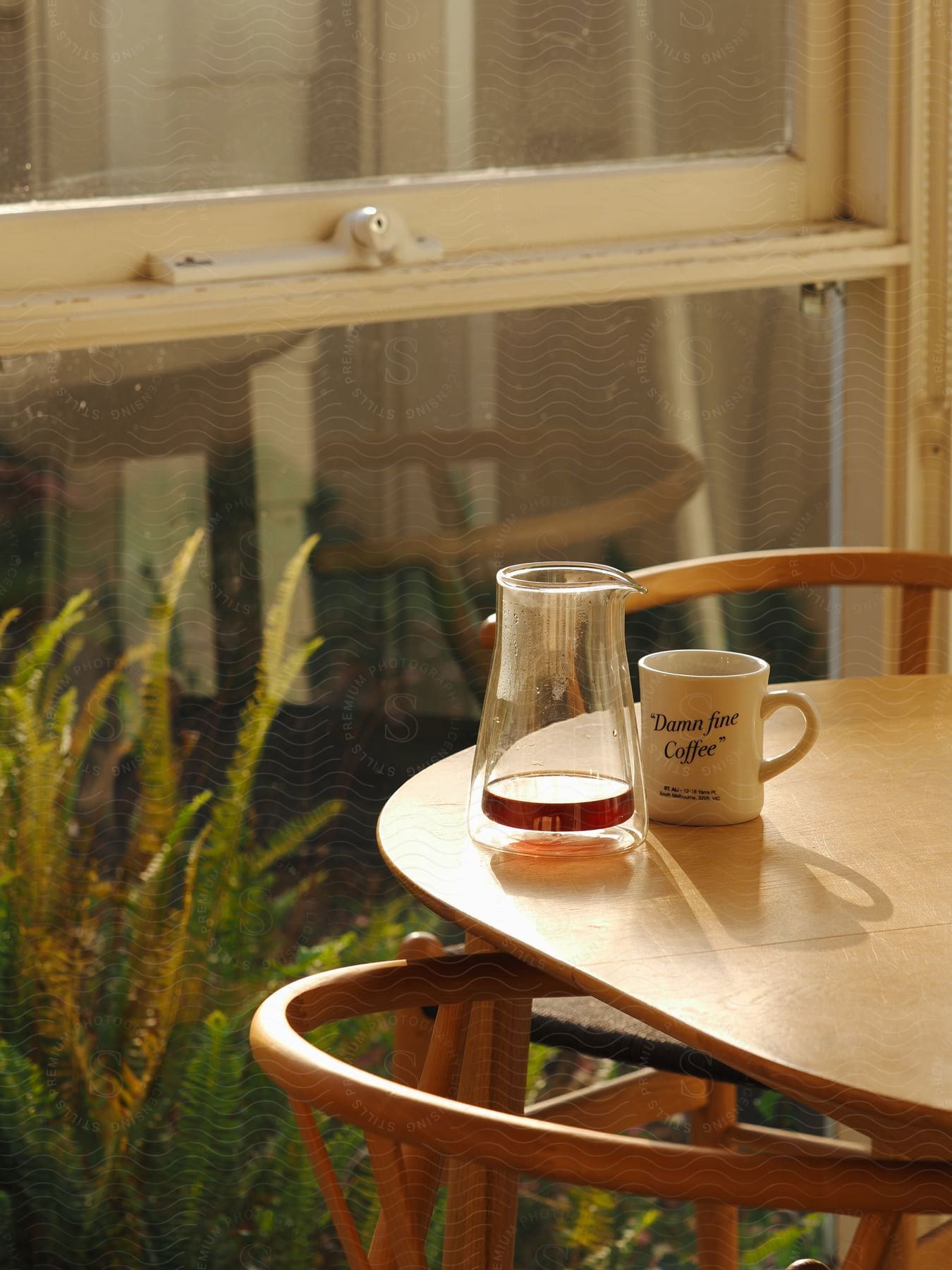 Pitcher and coffee cup sit on a table near the window next to the garden.