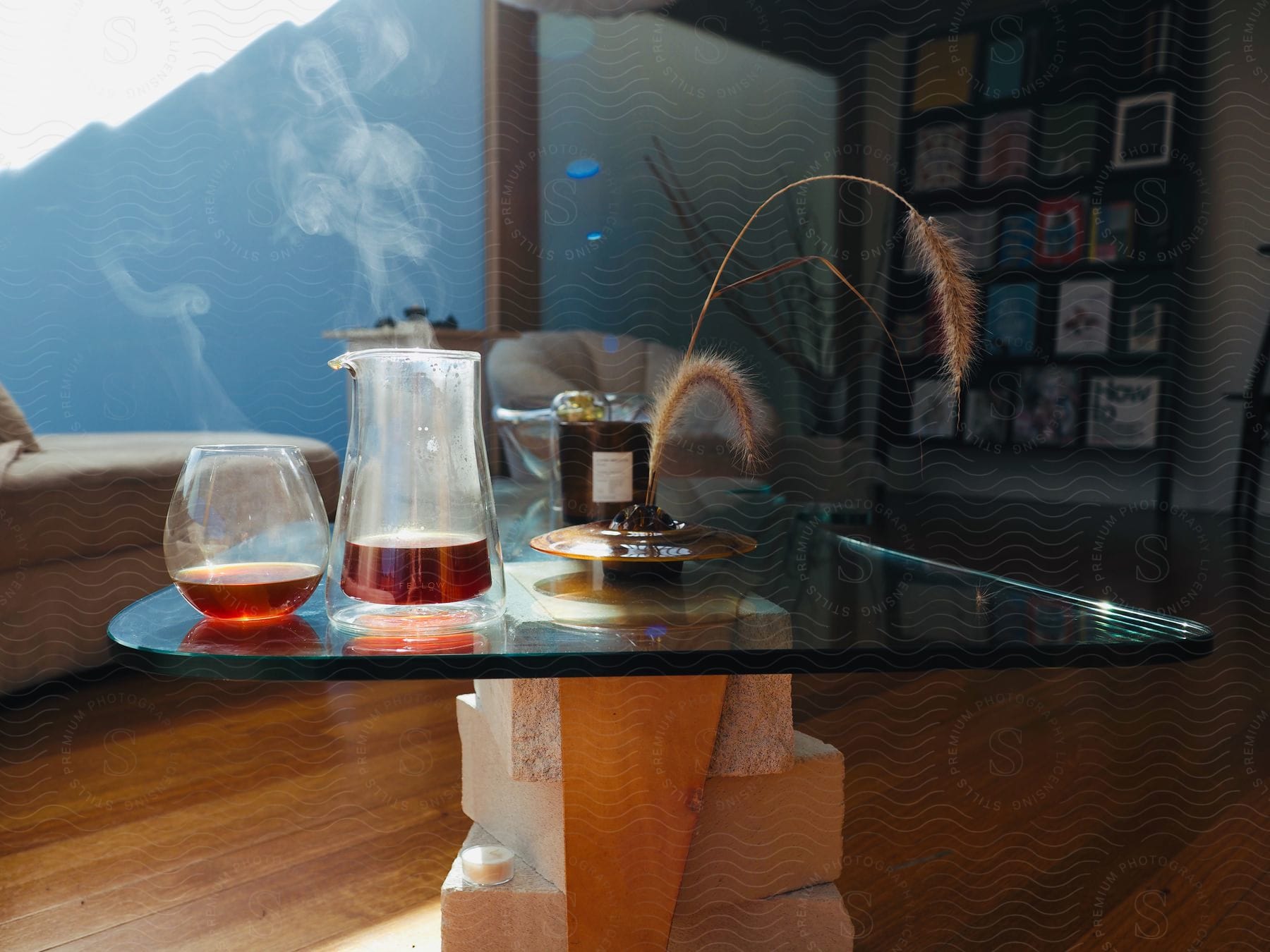 An alcoholic beverage sits on the corner of a glass coffee table in a living room.