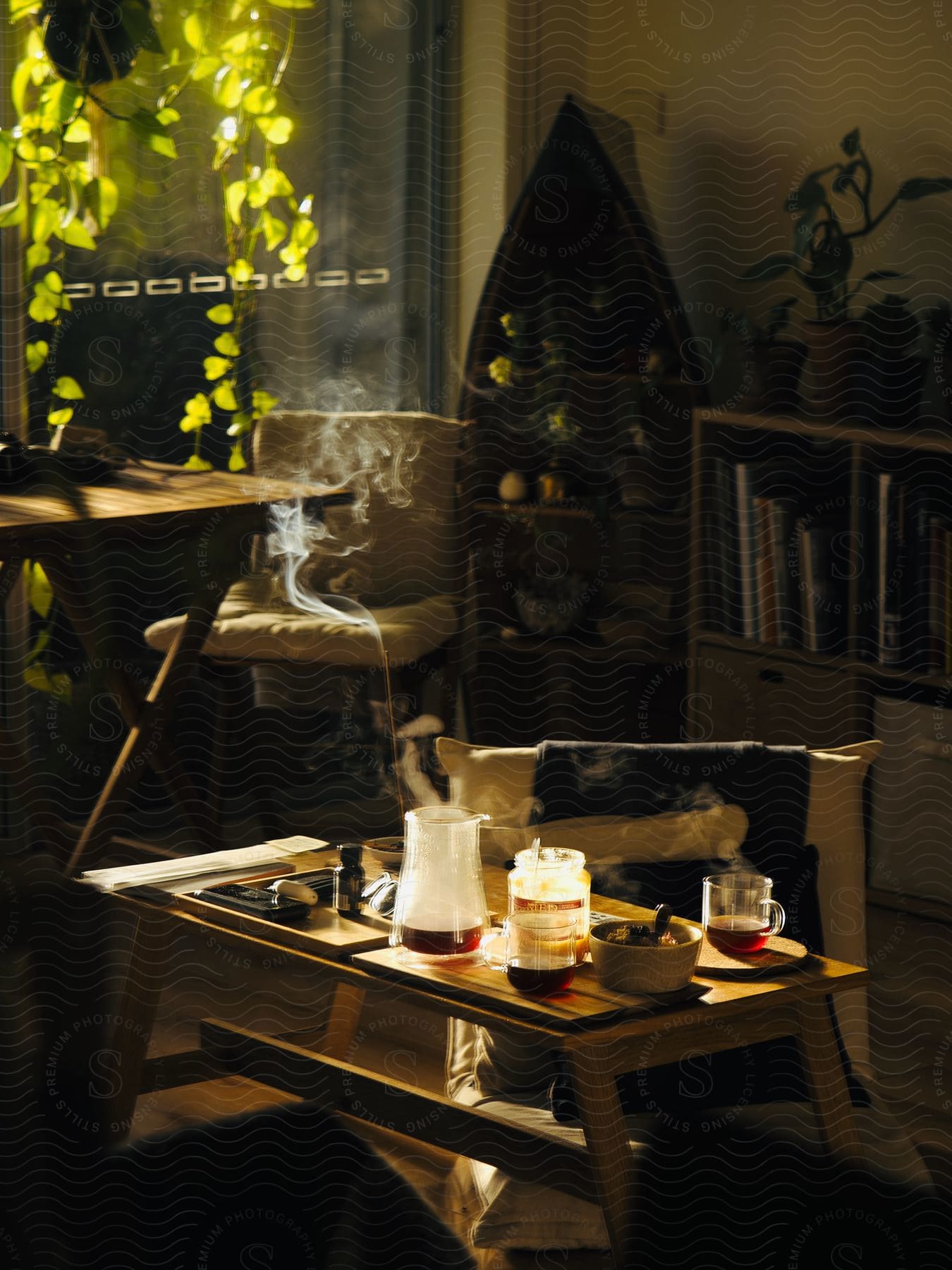 Indoor environment lit by sunlight, with a coffee table containing a jug, mug with tea and bowl, surrounded by plants and books.