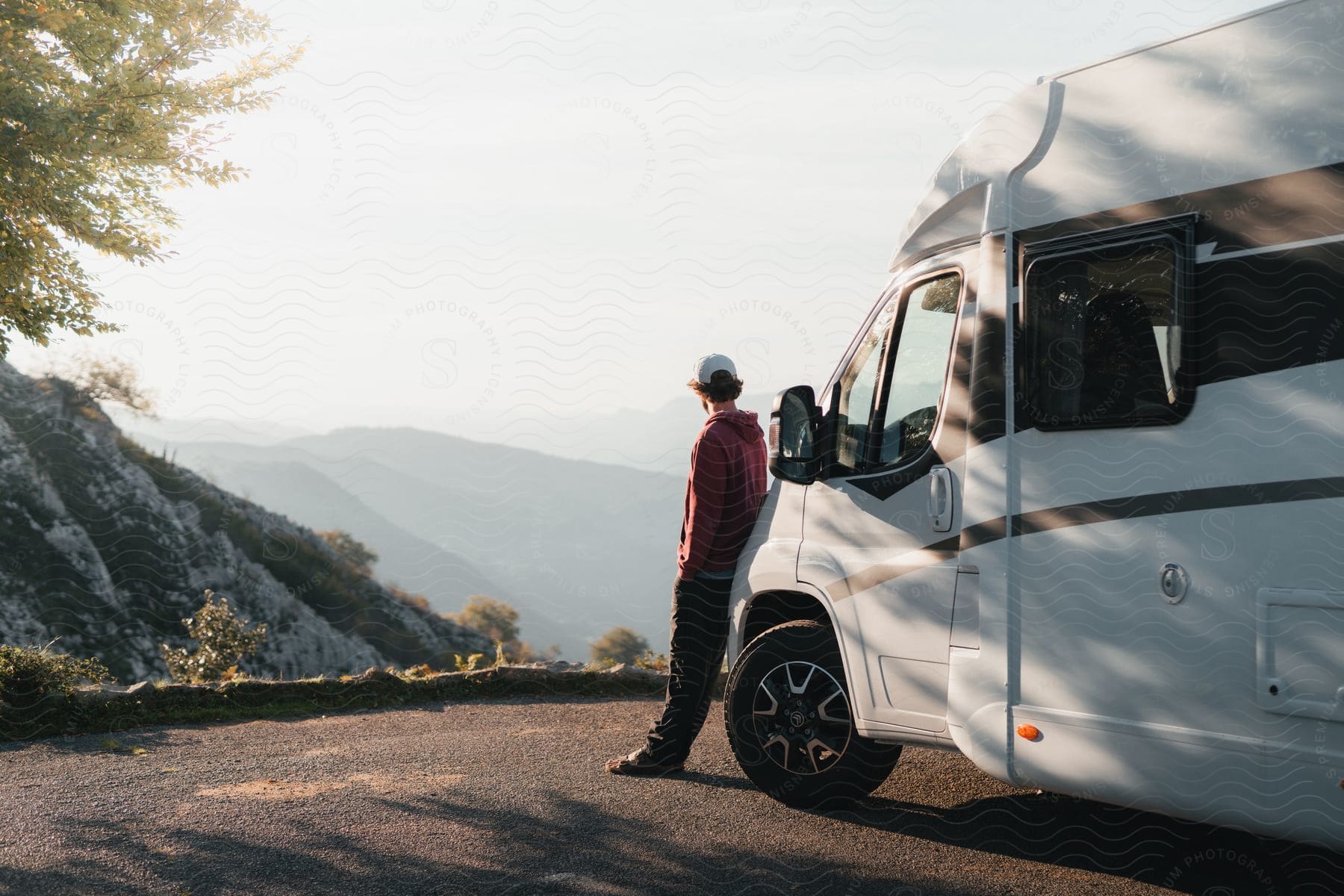 A man leans against an RV while looking out over a mountainous landscape.