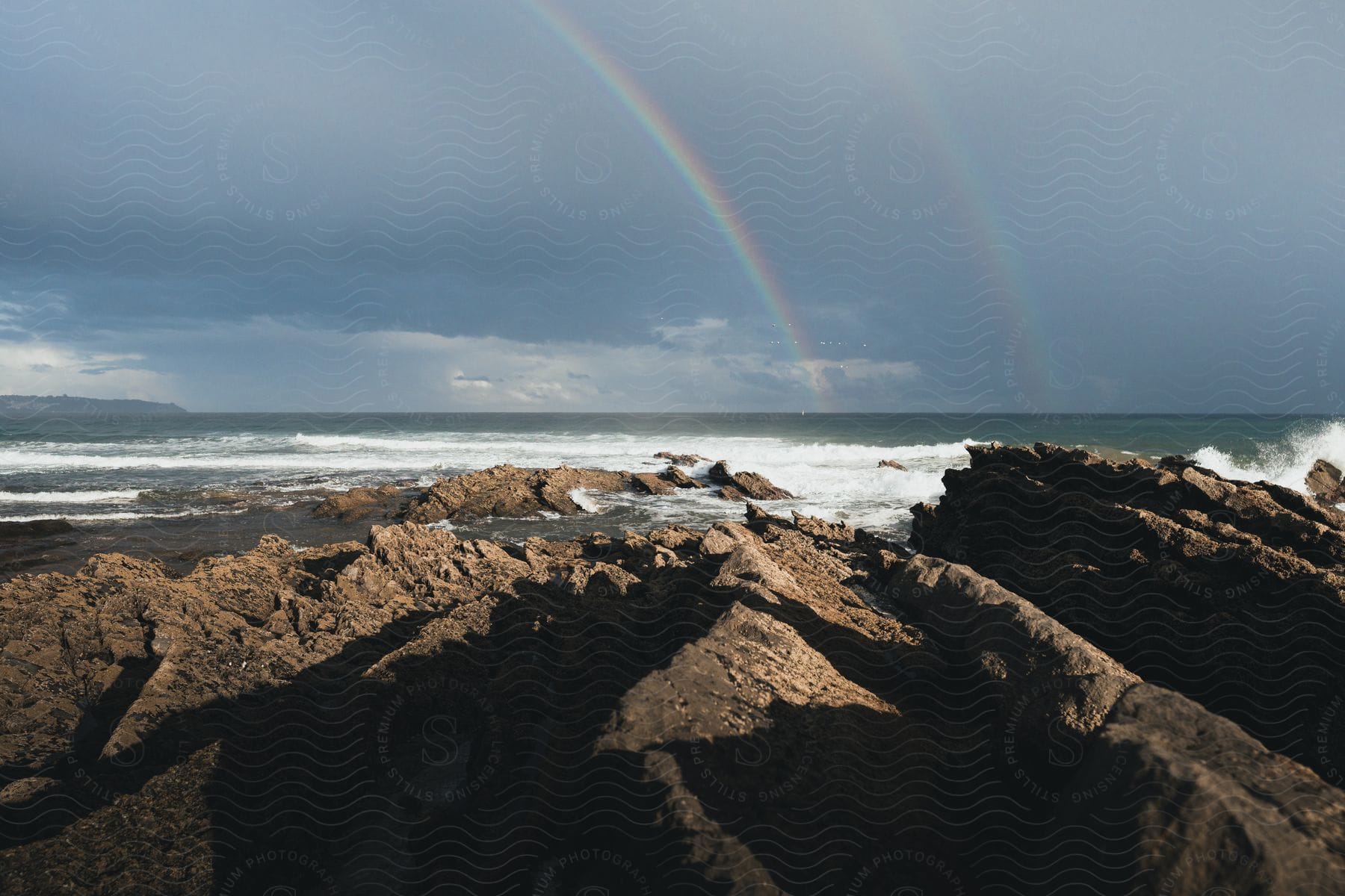 A landscape of a rocky shore and sea with rainbows in the background.