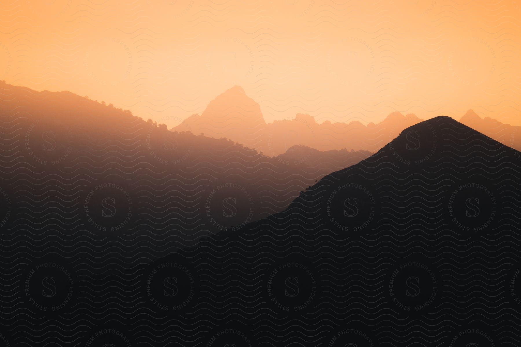 Silhouettes of mountain peaks against an orange sky at sunset.