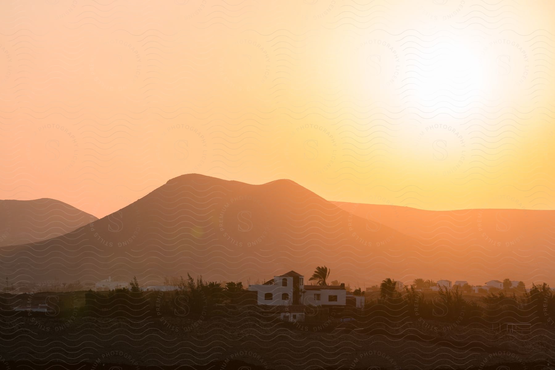 Houses in a rural area as the sun shines brightly over the mountains in a hazy sky