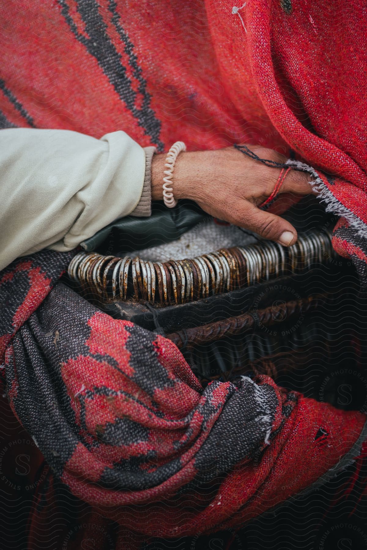 An old woman's hand on a basket parcially covered with a black and red blanket.