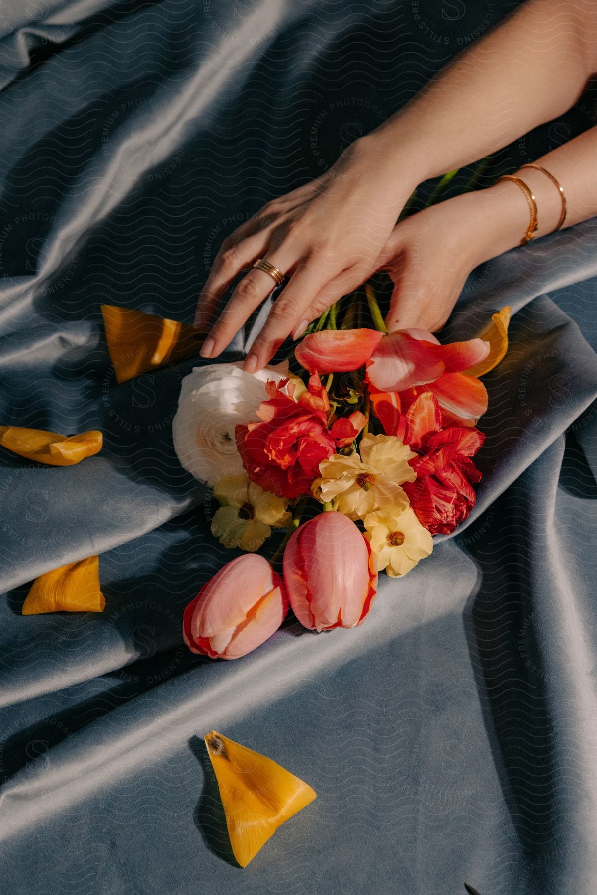 A woman holding a series of flowers while wearing a ring and an ankle bracelet.