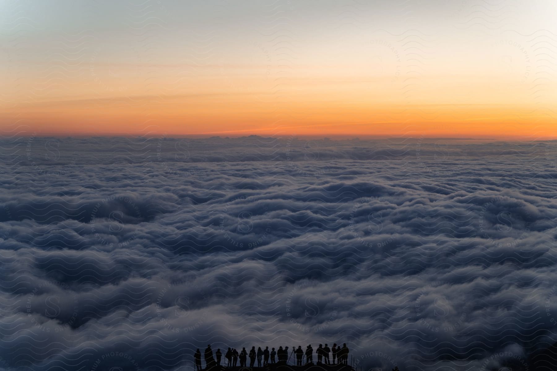 Silhouettes of a group of people overlayed on an aerial view of a cloud bank seen from above.