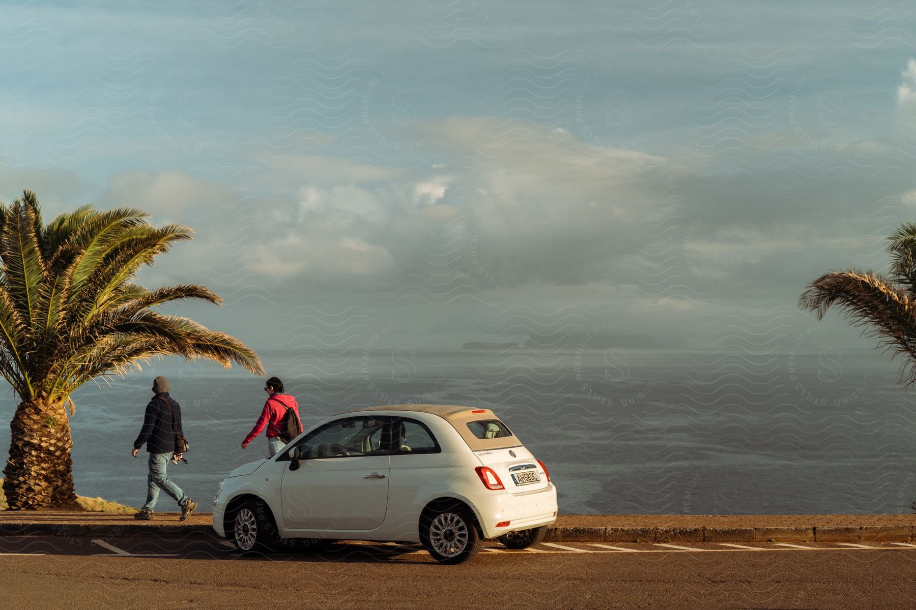 Two people walk near a parked automobile along the coast