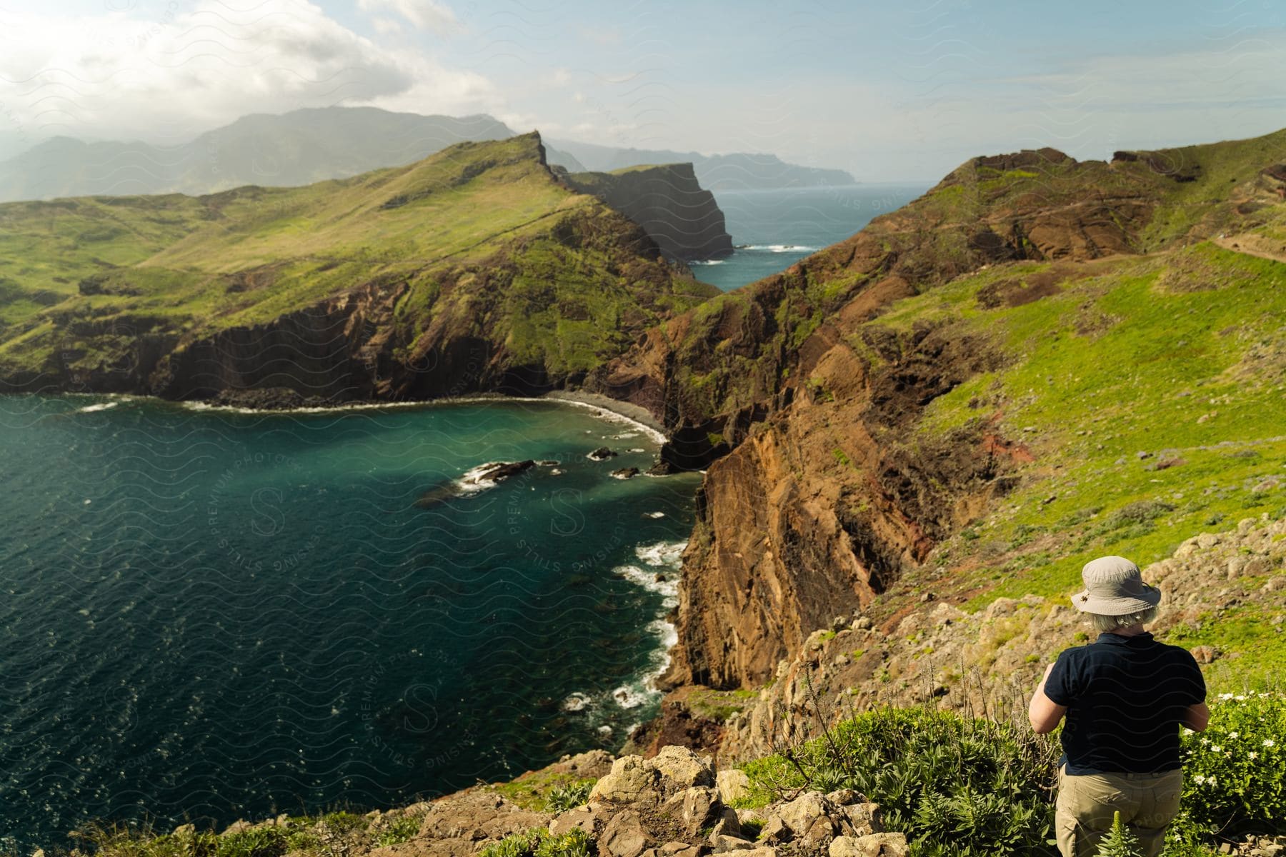 A person admires a breathtaking view of a coastal landscape, with steep cliffs and the blue ocean in the background.