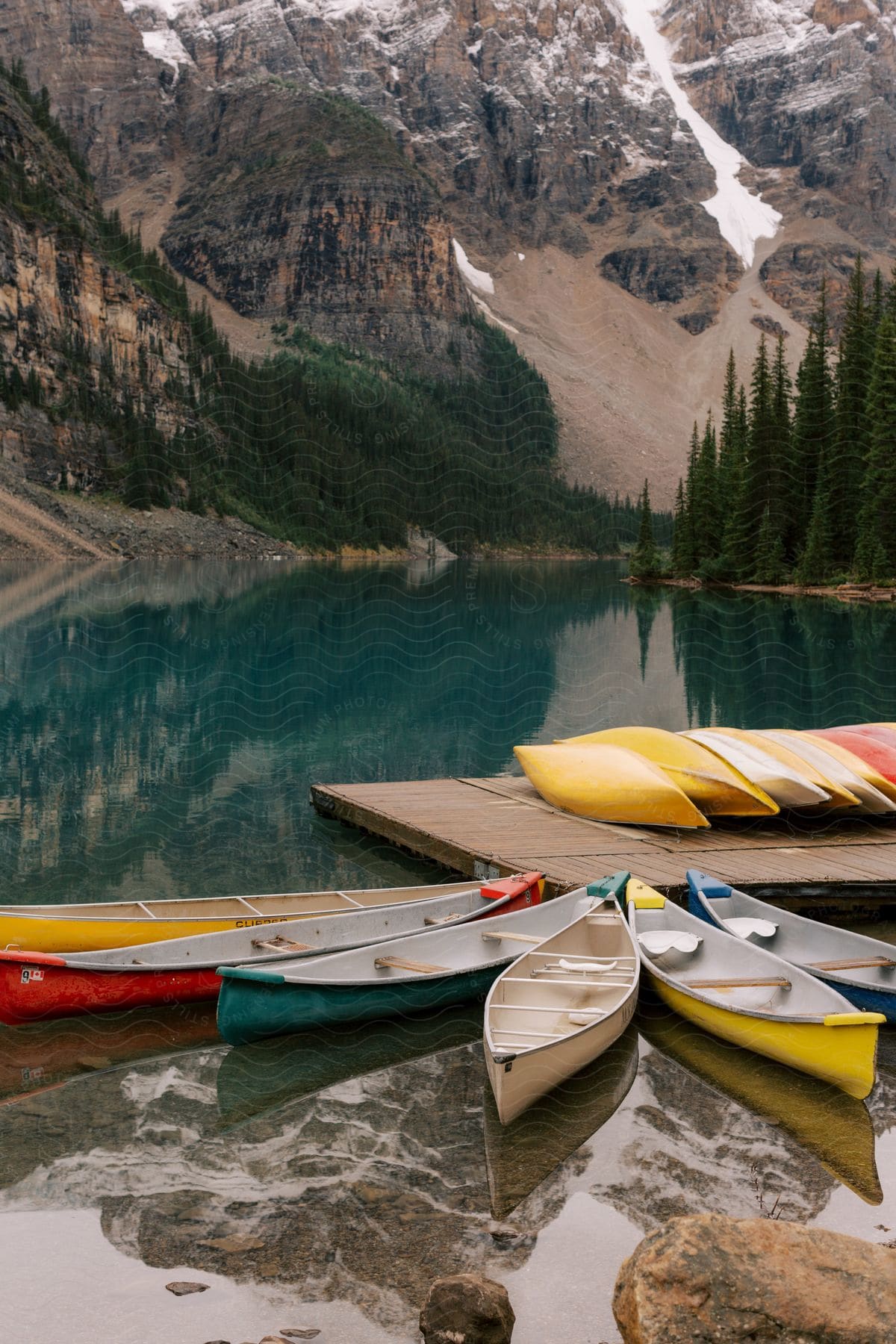 Canoes on the dock and in the water with forested mountains in the distance