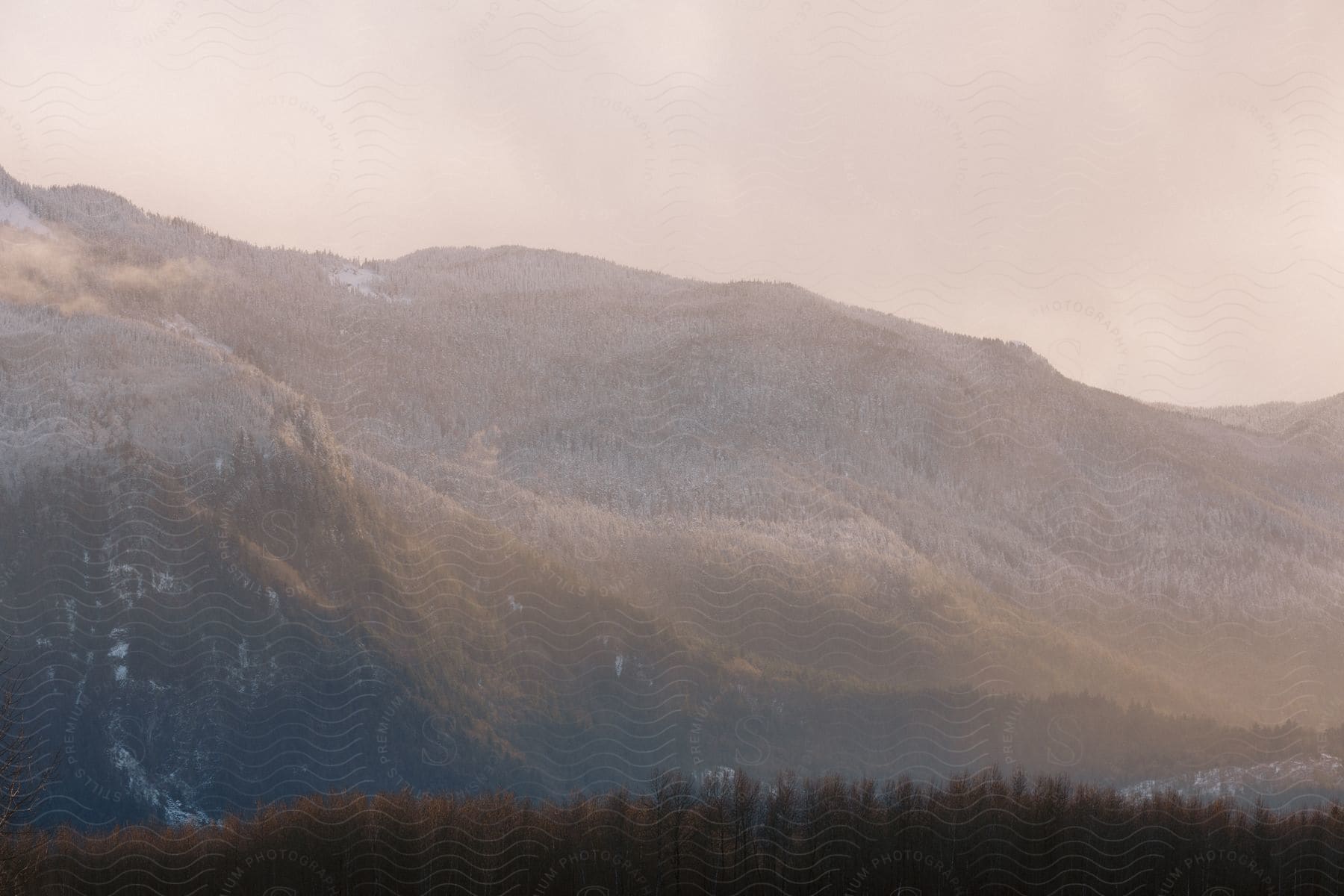 A mountain range is dusted with snow on a cloudy day.