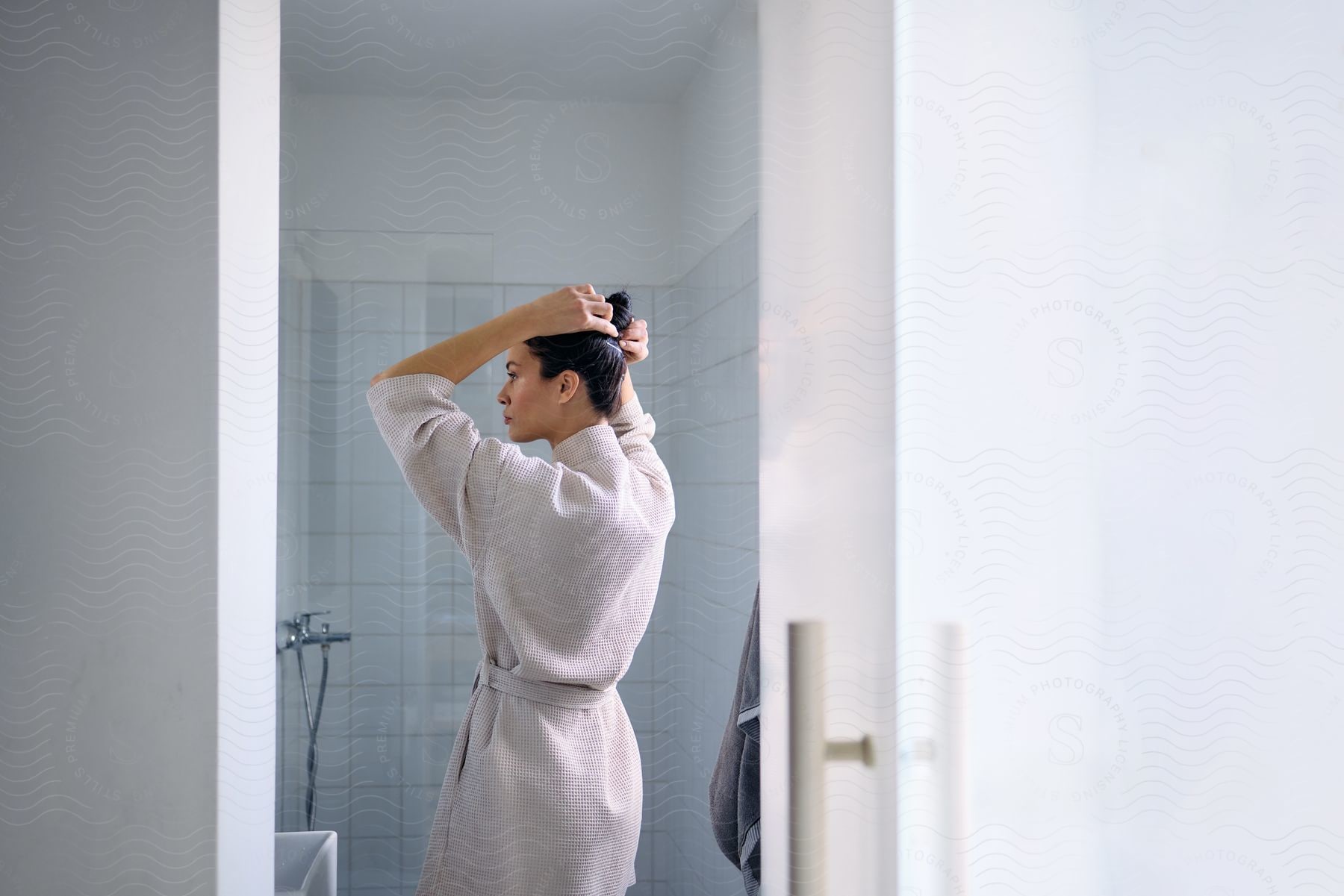 Woman wearing robe in bathroom puts up her hair.