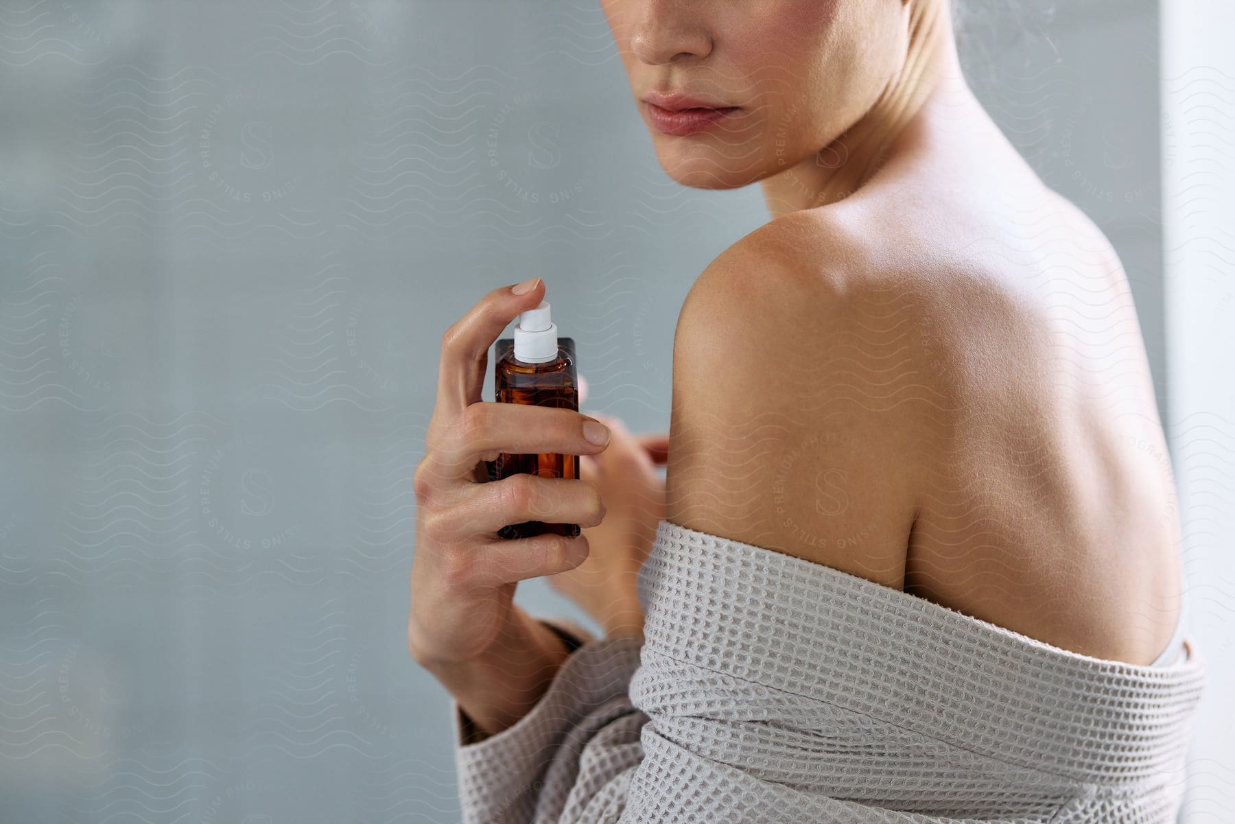 Woman in a robe holding a bottle product, focusing on her bare shoulder.