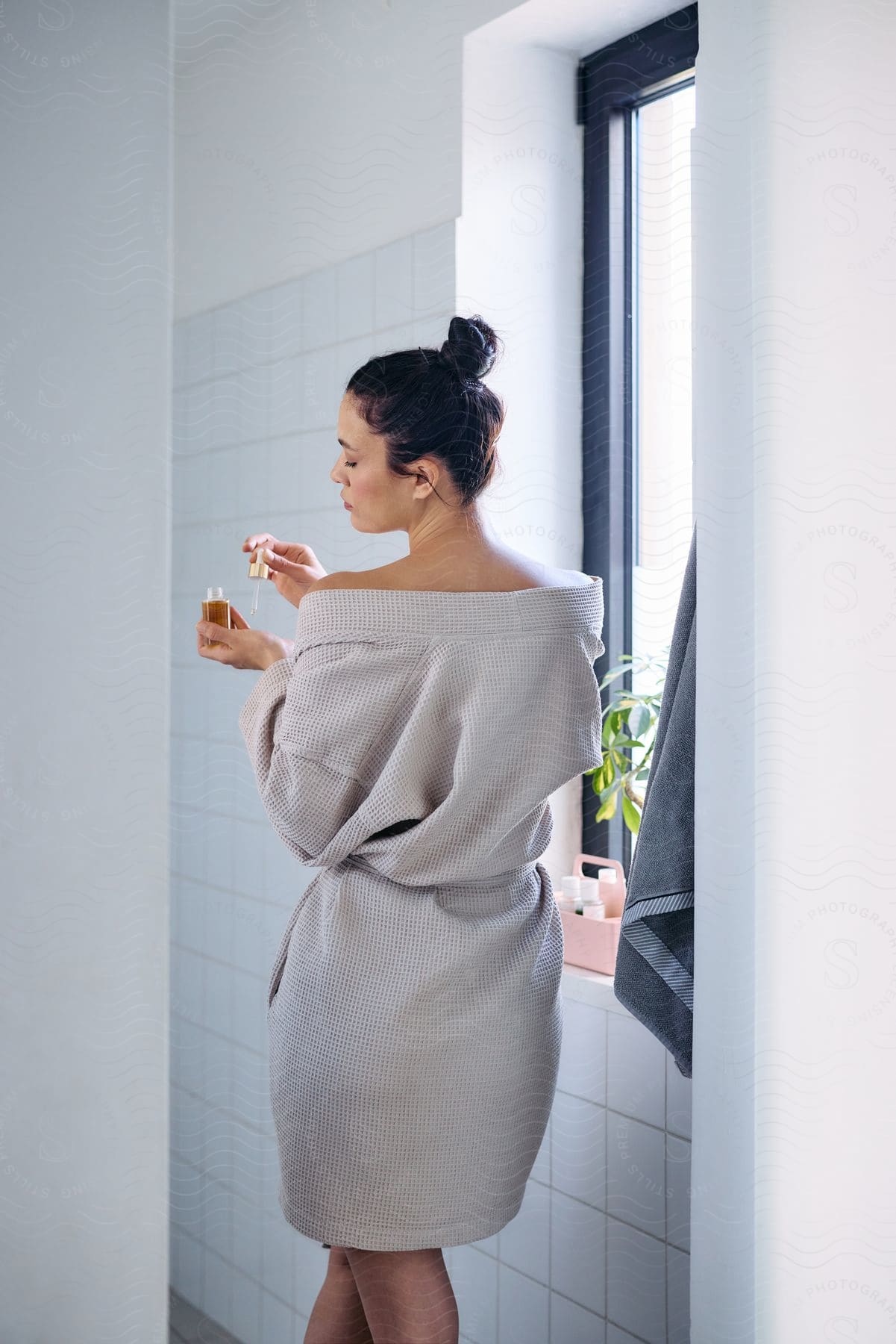 Woman from behind and in a bathrobe applying oil to her hand.