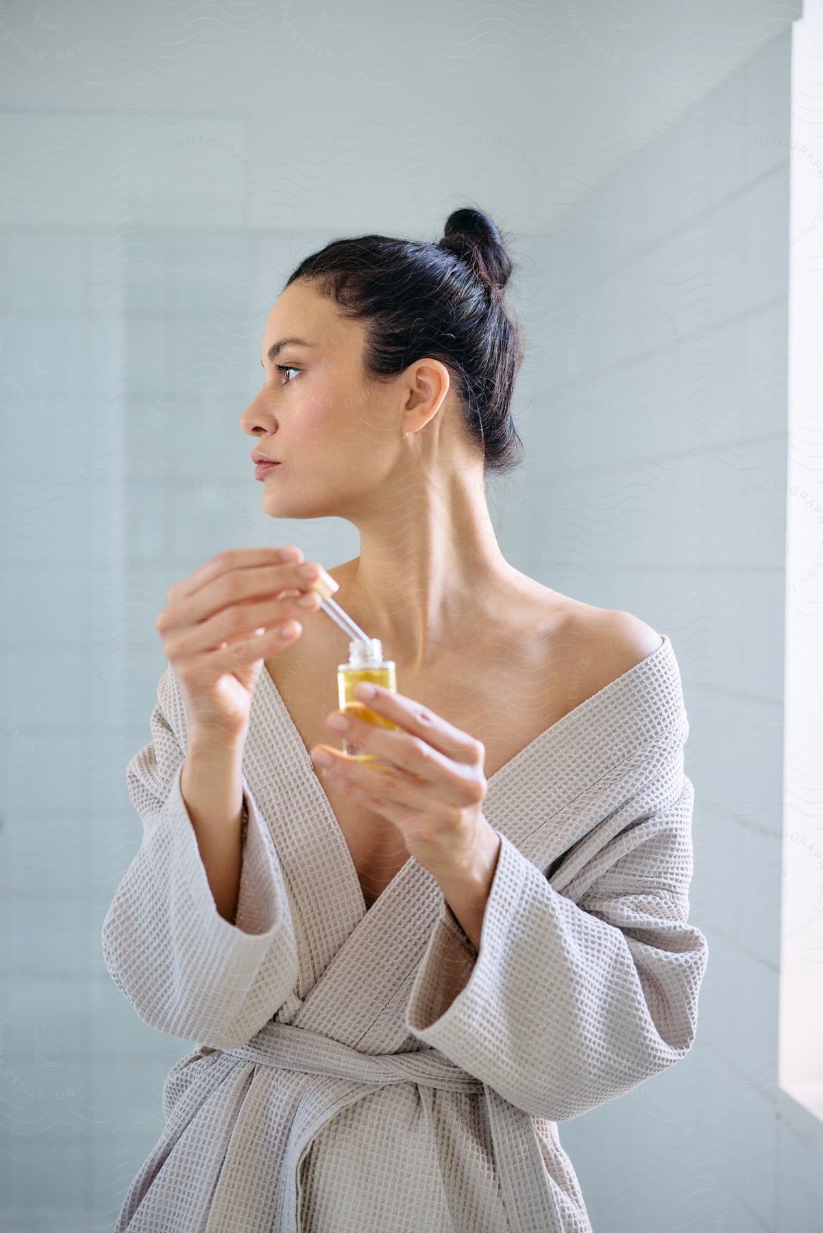 Woman in a bathrobe holding a serum oil in her hands.