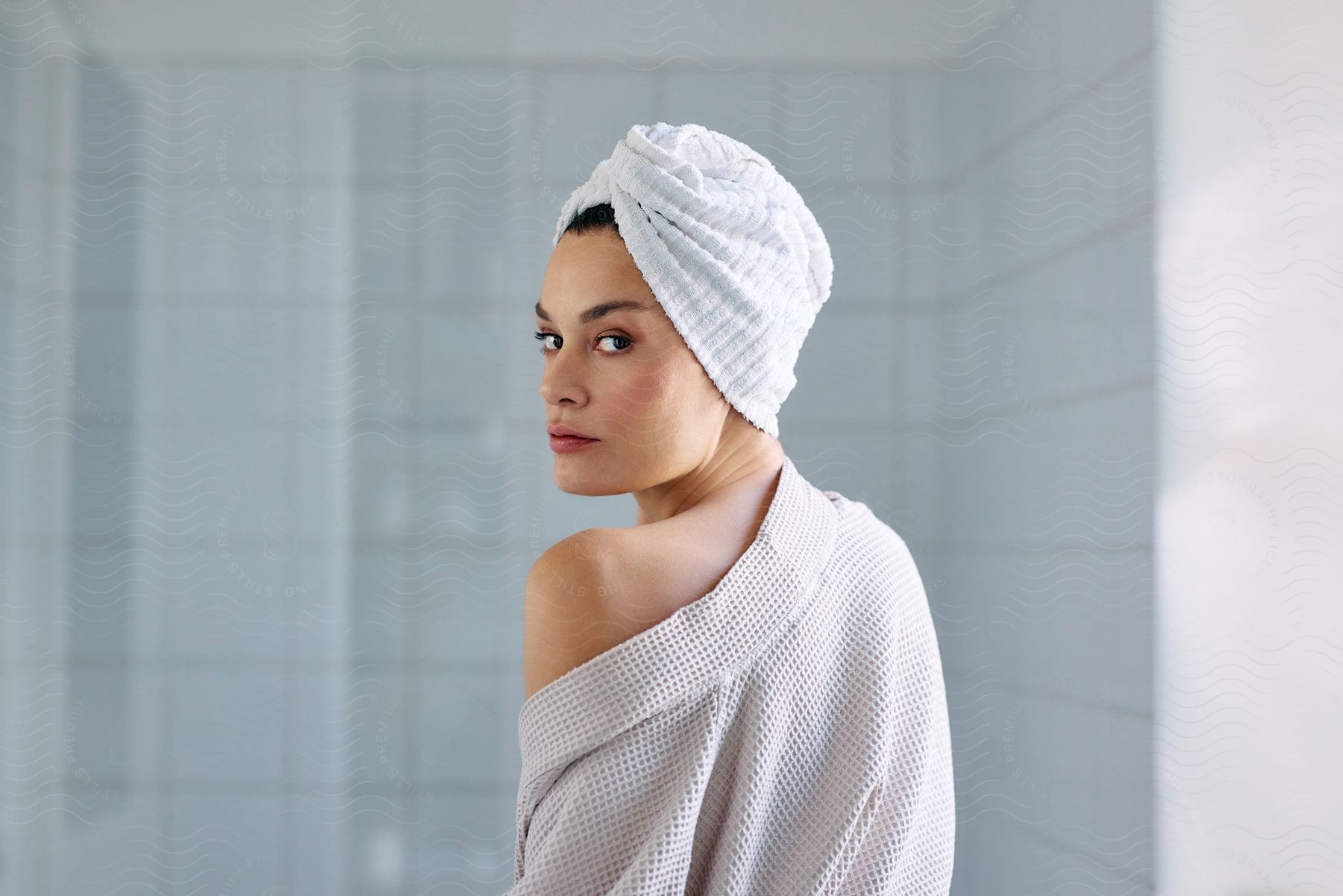 Woman wearing turban and robe looks over her shoulder while standing in the bathroom.