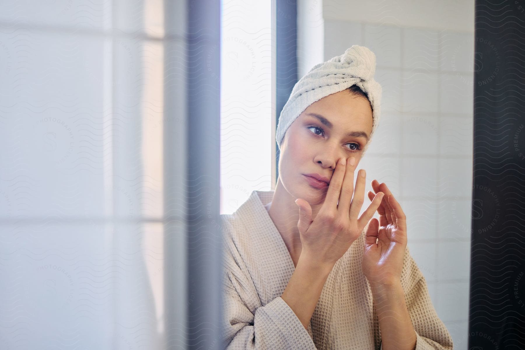 Woman in a bathrobe standing in the bathroom applying skin cream to her face