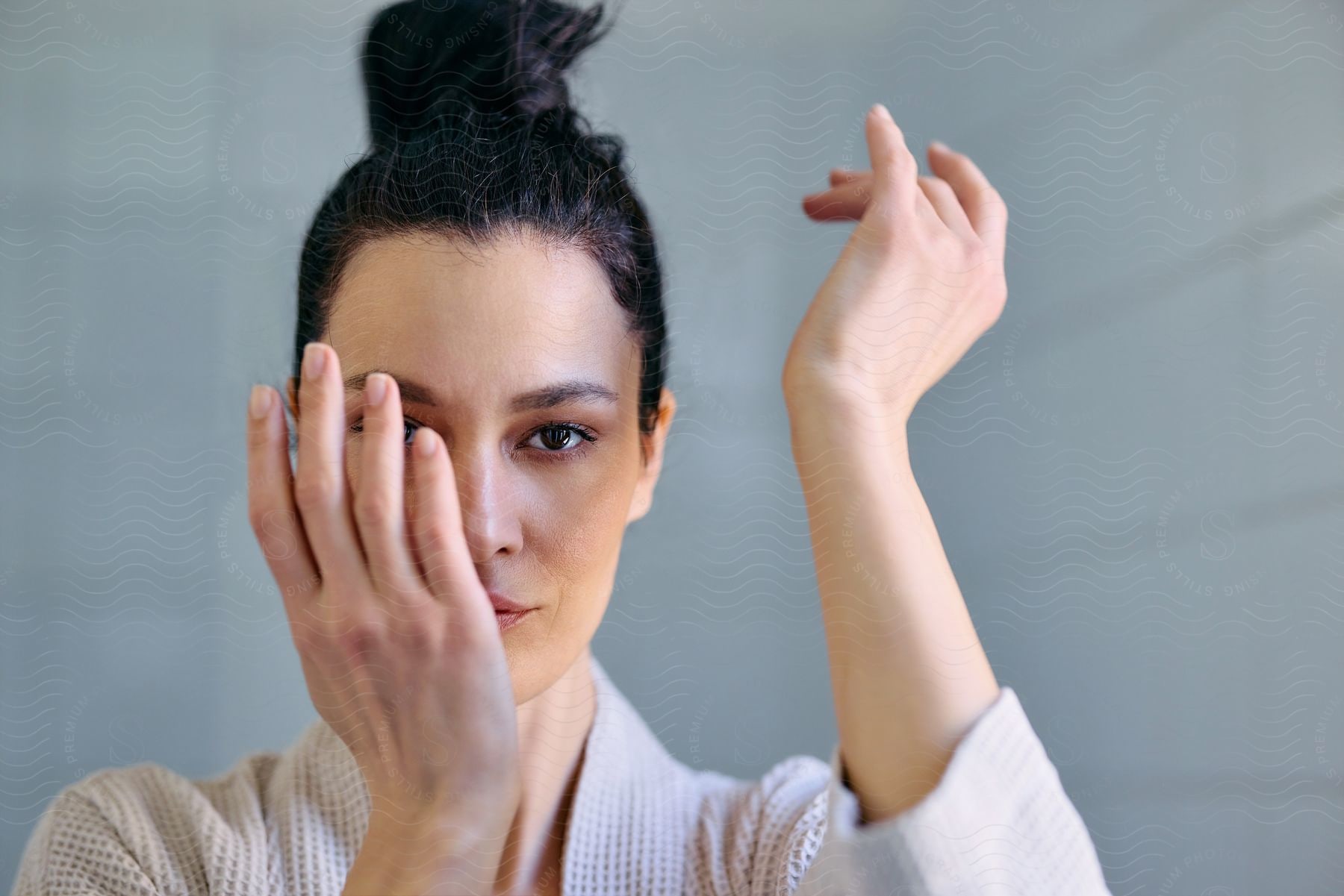 Woman with a bun hairstyle, her face partially obscured by her hand