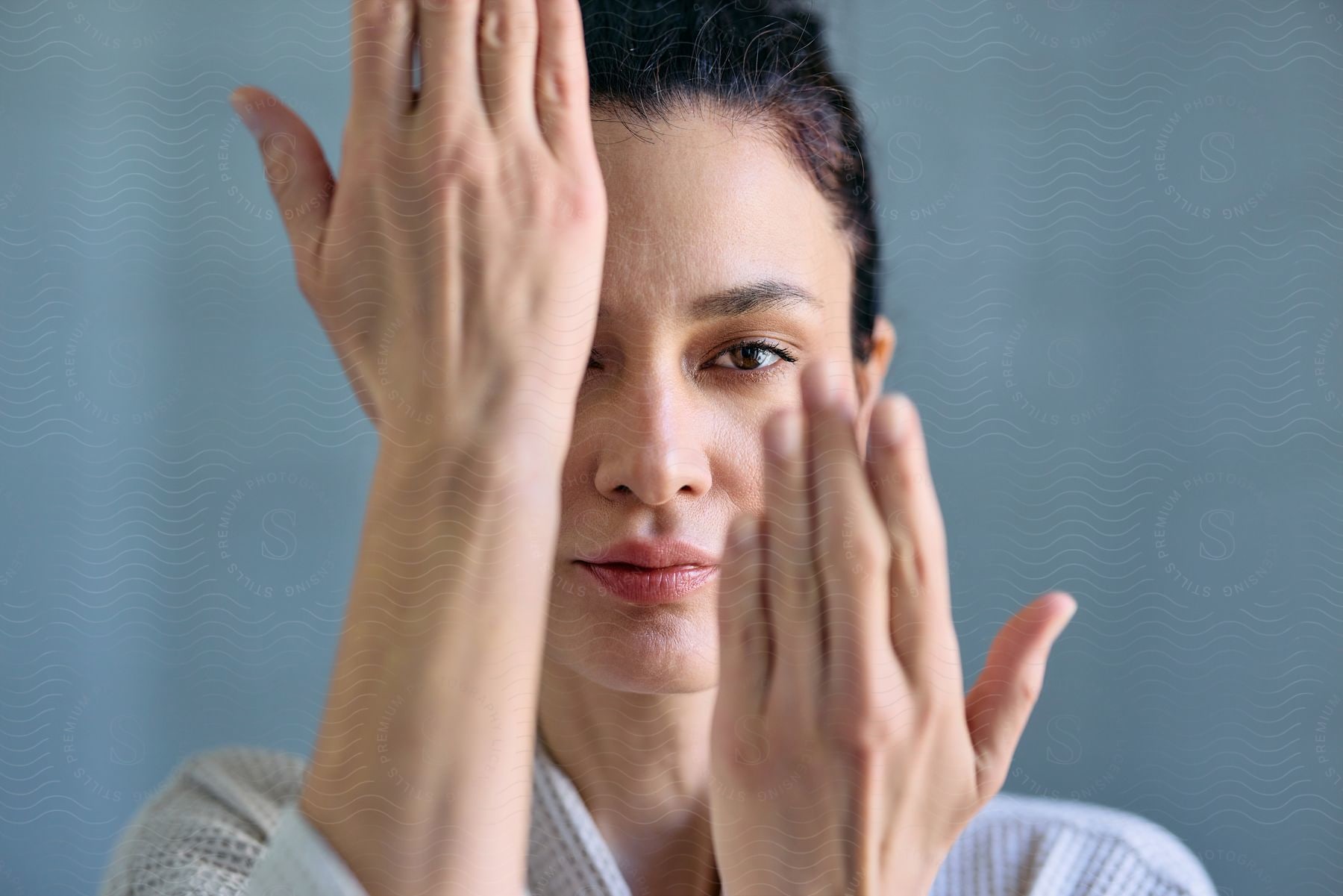 A woman wearing a bathrobe holds her hands up against her face in the bathroom