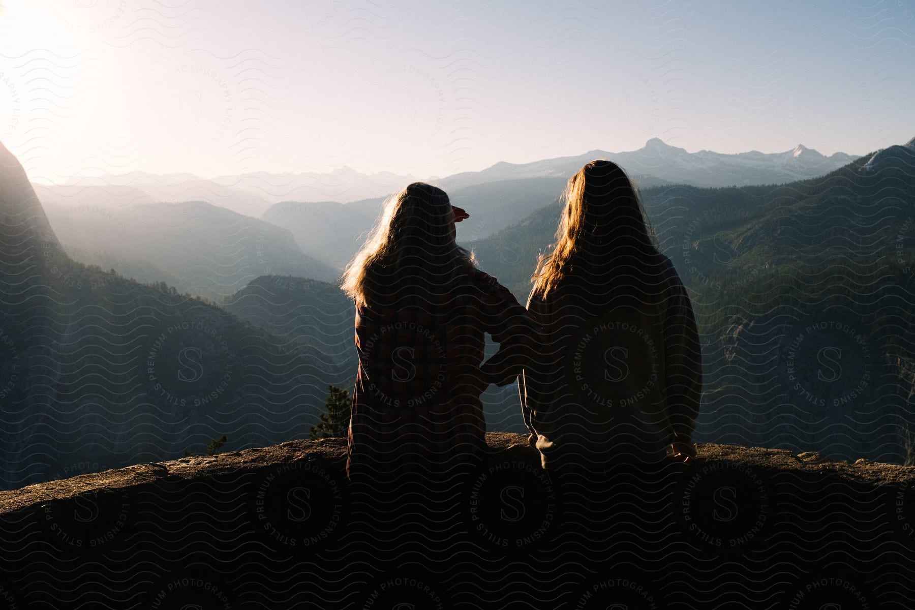 Two women stand on a balcony overlooking the mountains under a hazy sky