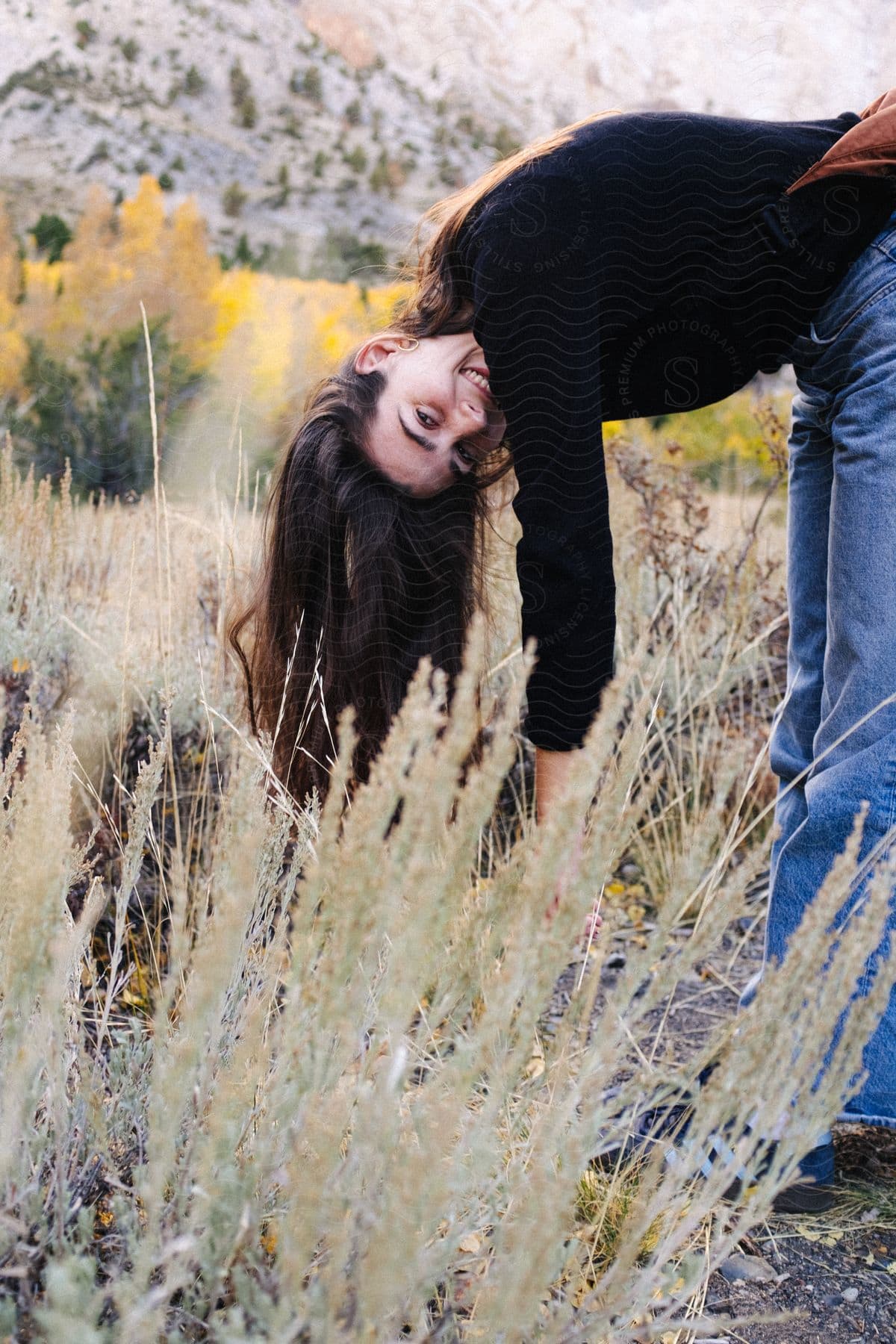 A woman smiles as she bends down among wheat plants during the day.