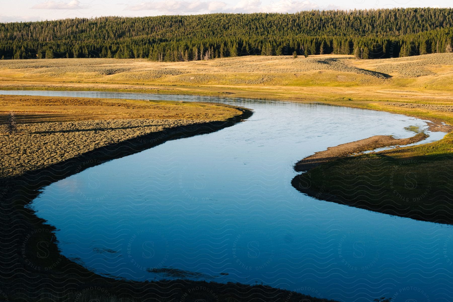 Winding river with calm waters surrounded by fields and wooded hills.