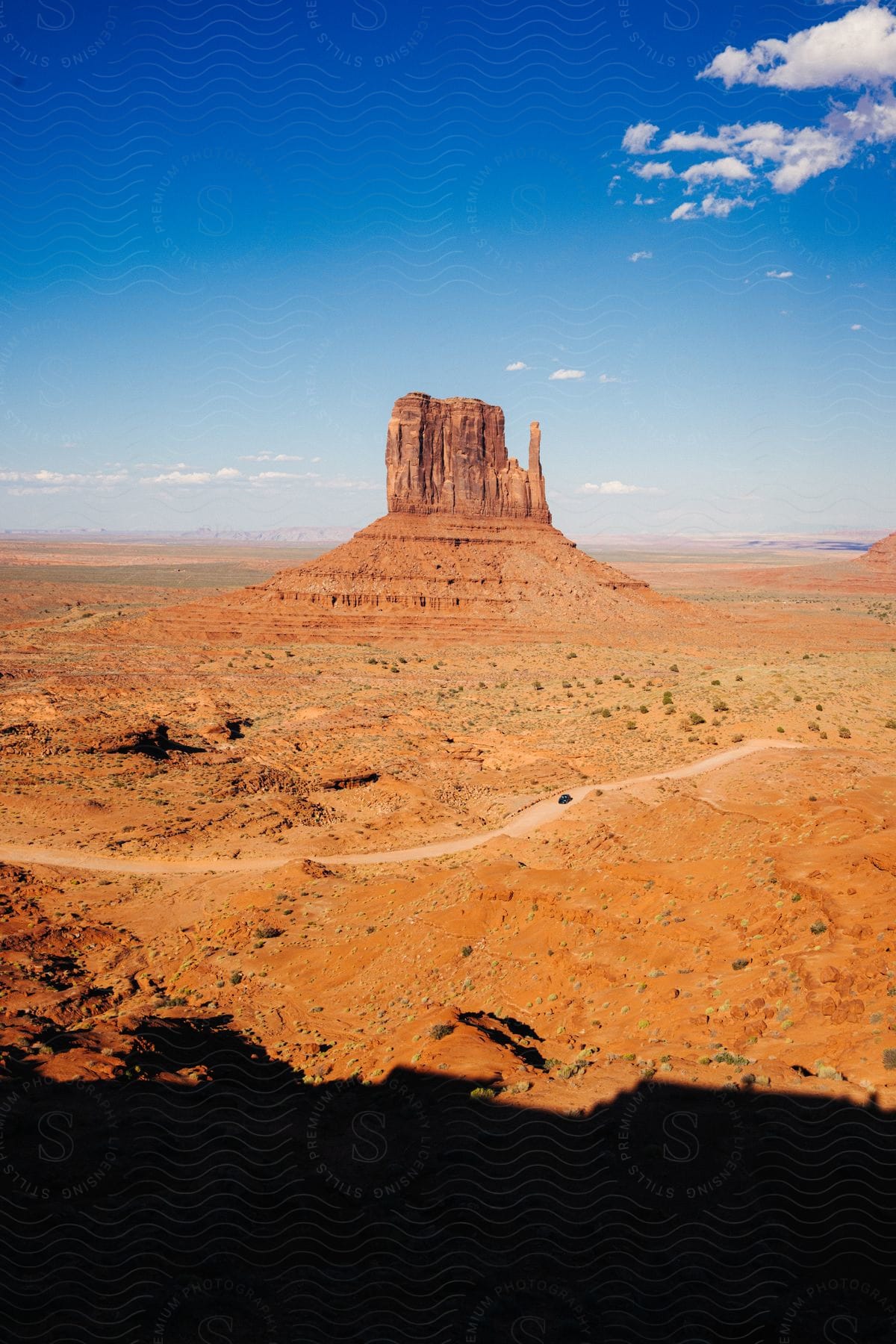 A majestic rock formation that rises above a vast arid landscape under a clear blue sky.