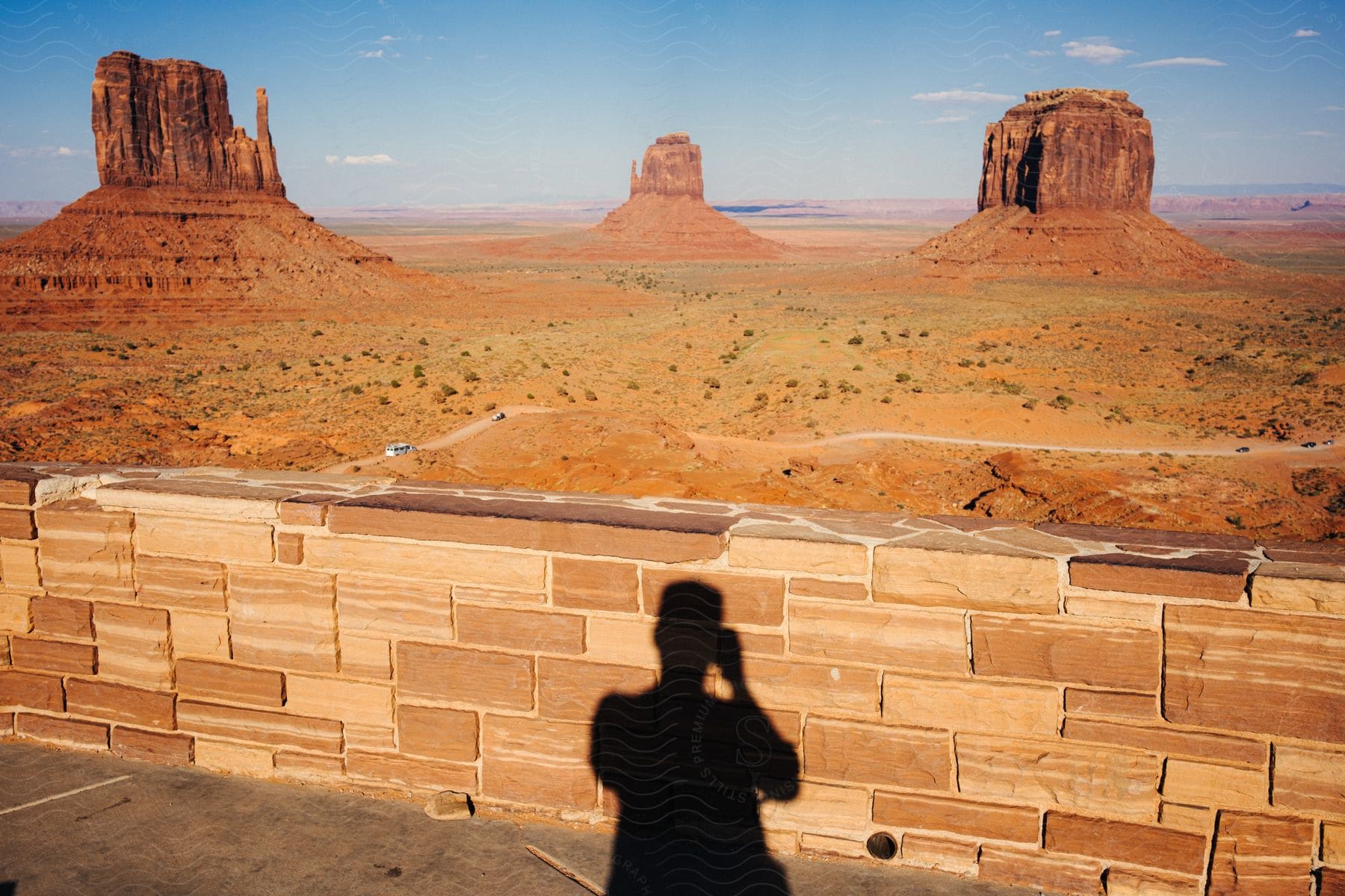 Shadow Of A Person In The Foreground With Two Prominent Buttes Of Monument Valley In The Background Under A Clear Sky