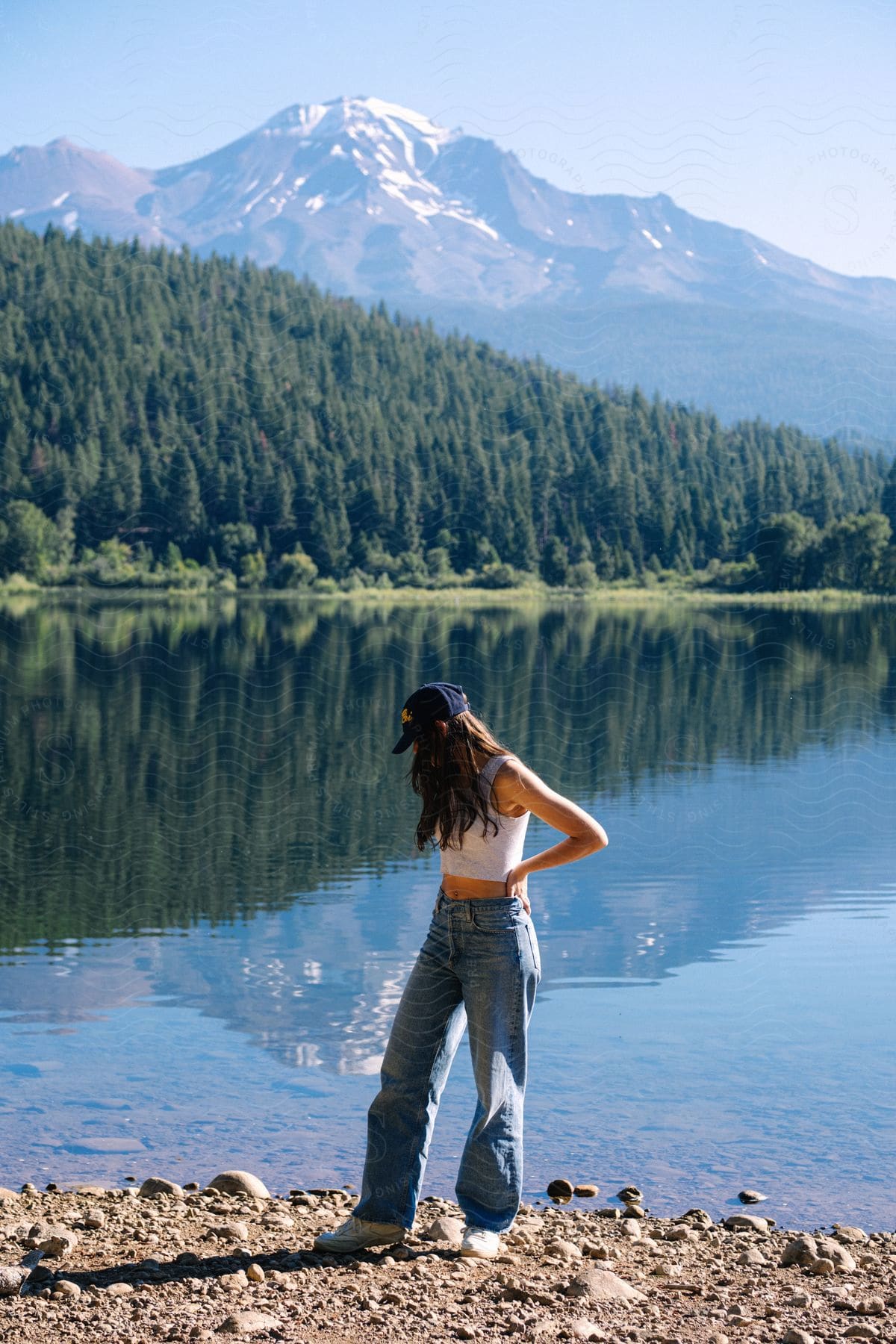 Woman stands along the coast with forested mountains across the river