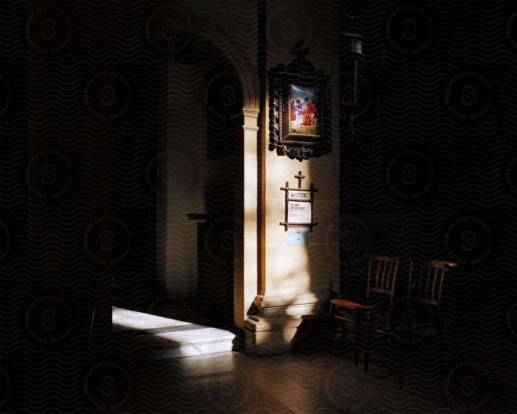 A serene church interior with sunlight streaming through an archway, illuminating a religious painting and a notice board on the wall.