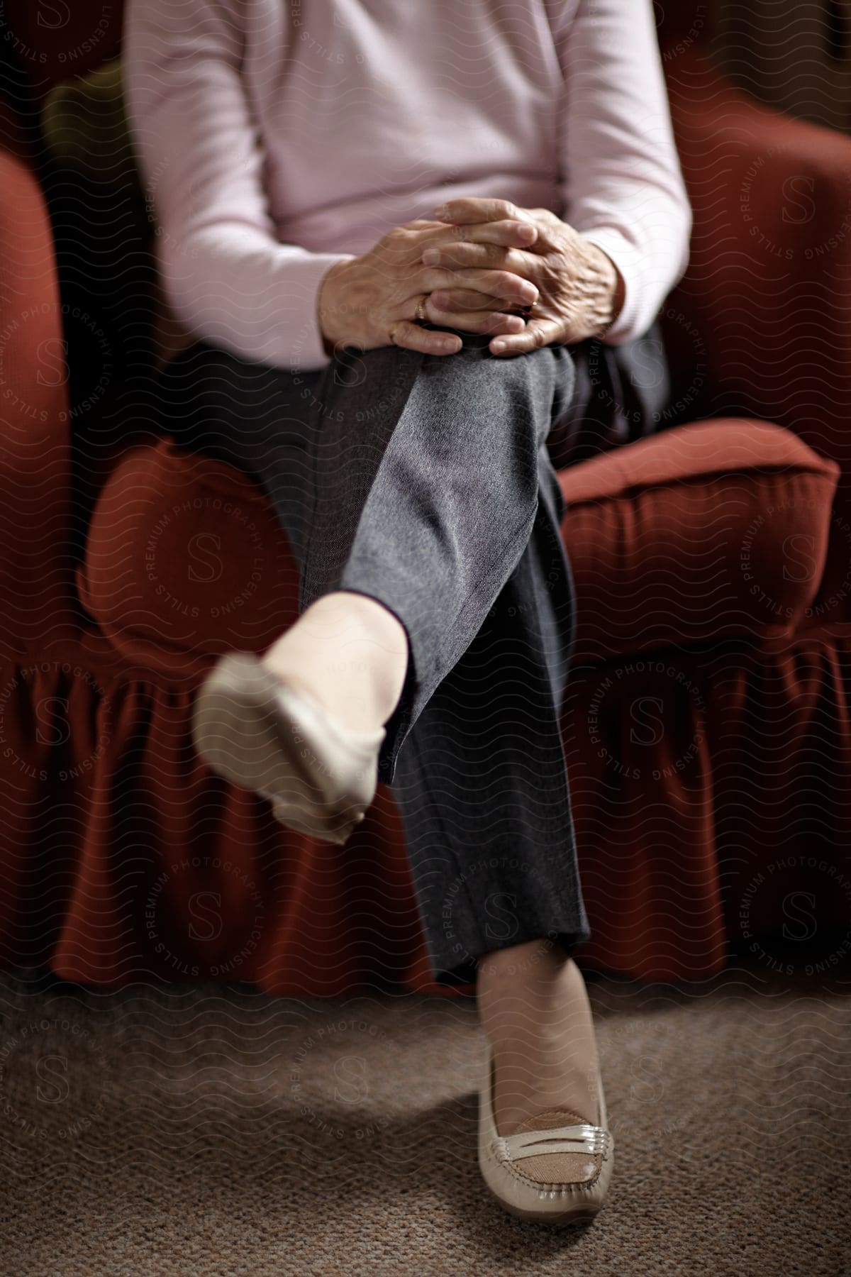 The person is sitting in a red armchair, with their hands crossed on their knees, in a comfortable and welcoming environment.