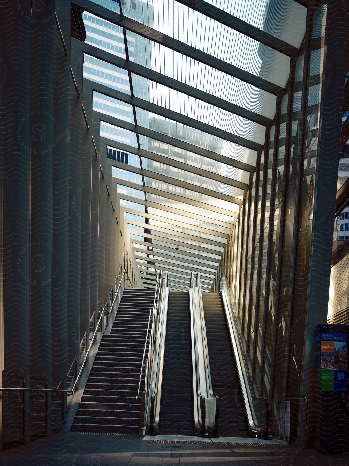 Staircase and escalators leading up to a modern building with glass ceiling and walls, allowing natural light to stream through.